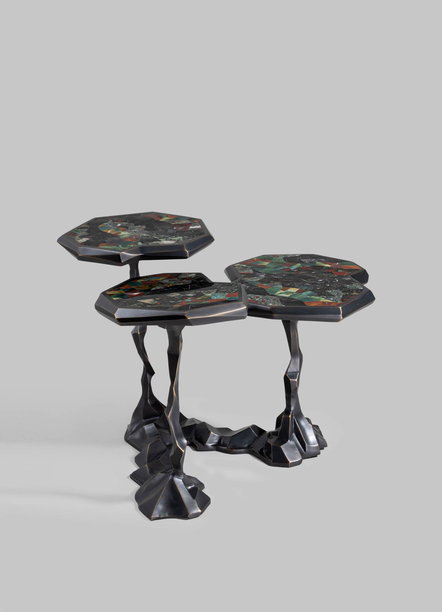 A set of three nesting side tables with irregular, sculptural metal bases in a dark finish and tabletops featuring colorful mosaic patterns in shades of green, red, black, and metallic accents.