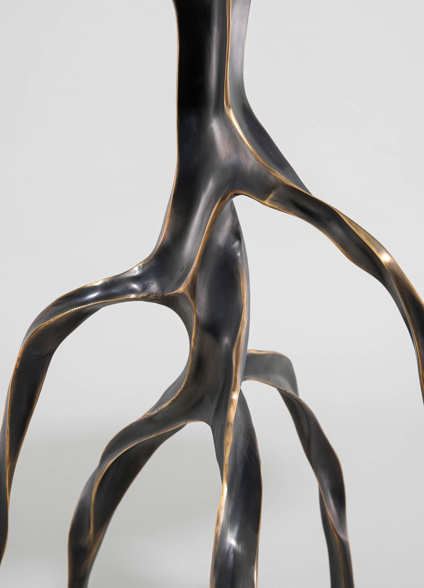 Sculptural table leg made of black metal with gold-toned accents, featuring organic, flowing shapes and a smooth finish, suitable for contemporary furniture design.