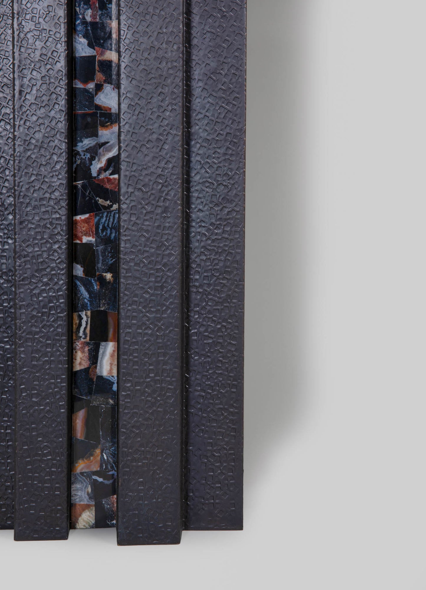 Textured dark grey panels with a geometric embossed pattern, featuring a vertical strip of multi-colored marble inlays with shades of black, white, red, and tan. The materials include metal and marble, with a contemporary and artisanal style.