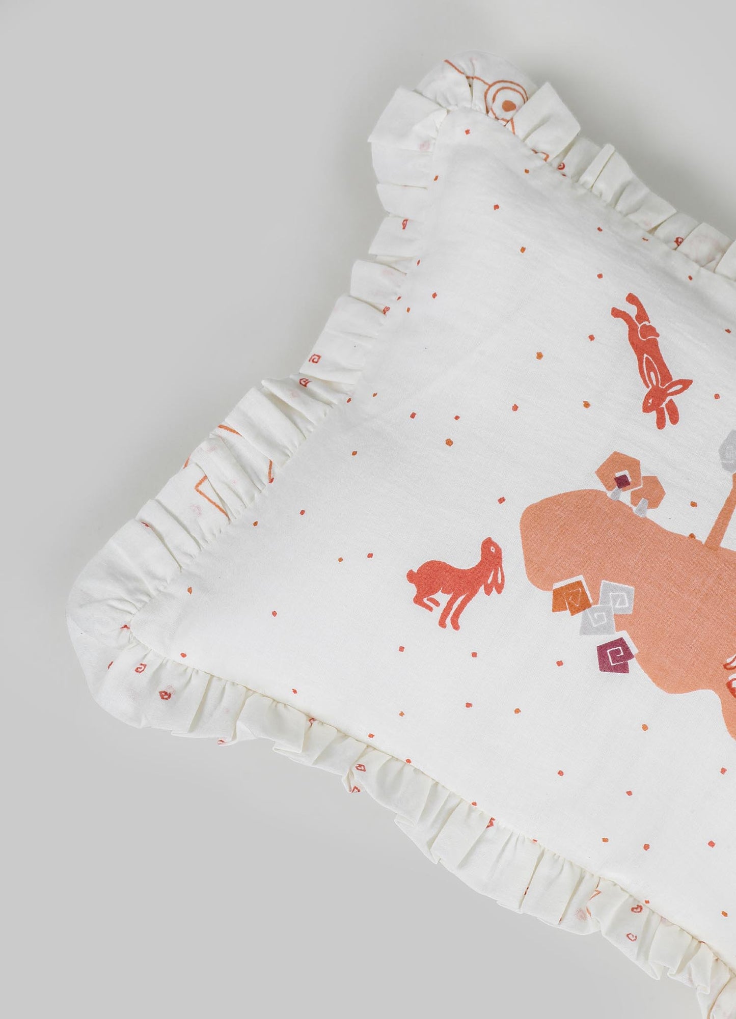 A white fabric baby blanket with ruffled edges features orange and pink animal and geometric motifs, including rabbits and cubes, arranged on a flat surface.