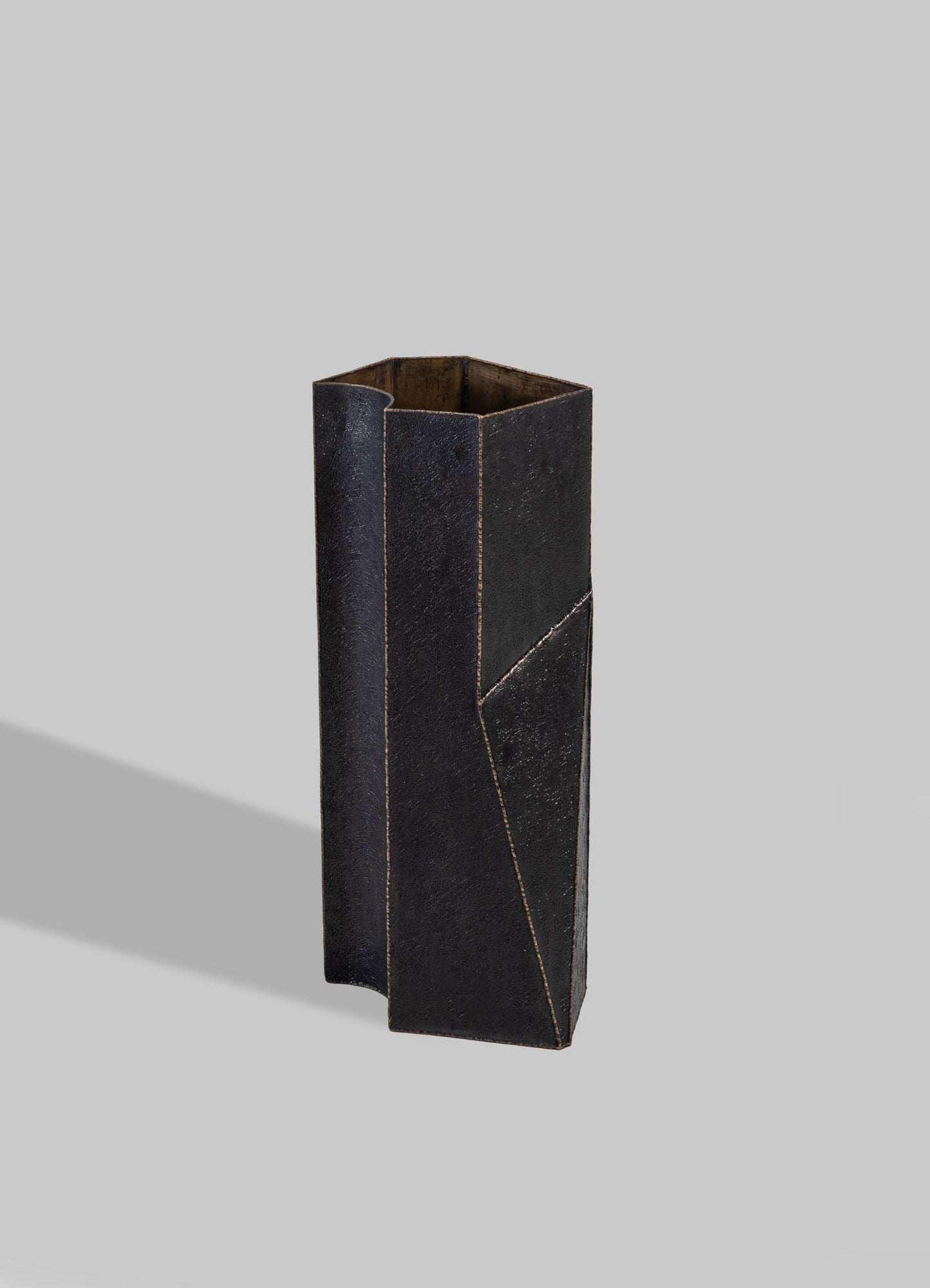 A tall, rectangular vase with a black, textured surface and geometric lines, made of wood or ceramic with metallic gold accents.