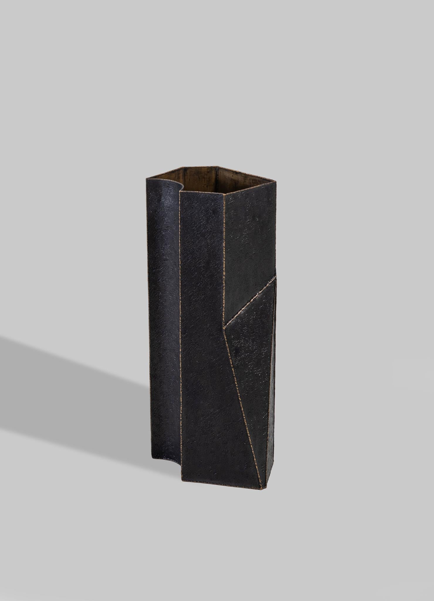 A tall, rectangular vase with a black, textured surface and geometric lines, made of wood or ceramic with metallic gold accents.