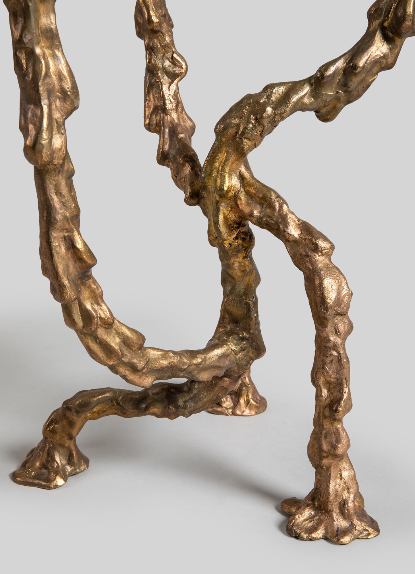 A close-up of a sculptural decorative piece made of textured metal with a golden-bronze finish, featuring organic, twisted shapes and irregular surface details.
