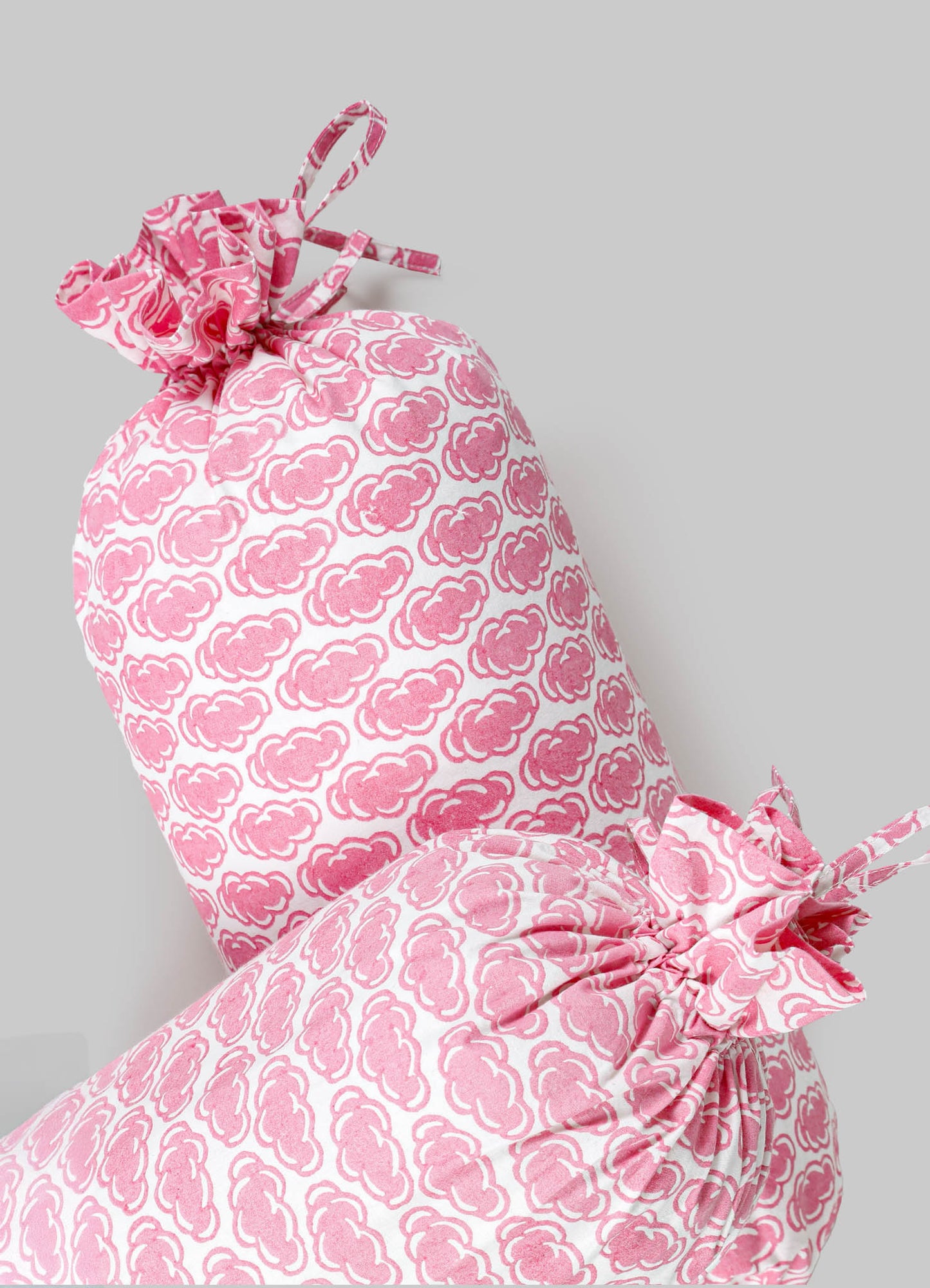 Pink and white fabric cushions with a repeating cloud-like pattern, tied at the edges with matching fabric bows, made from soft textile material.
