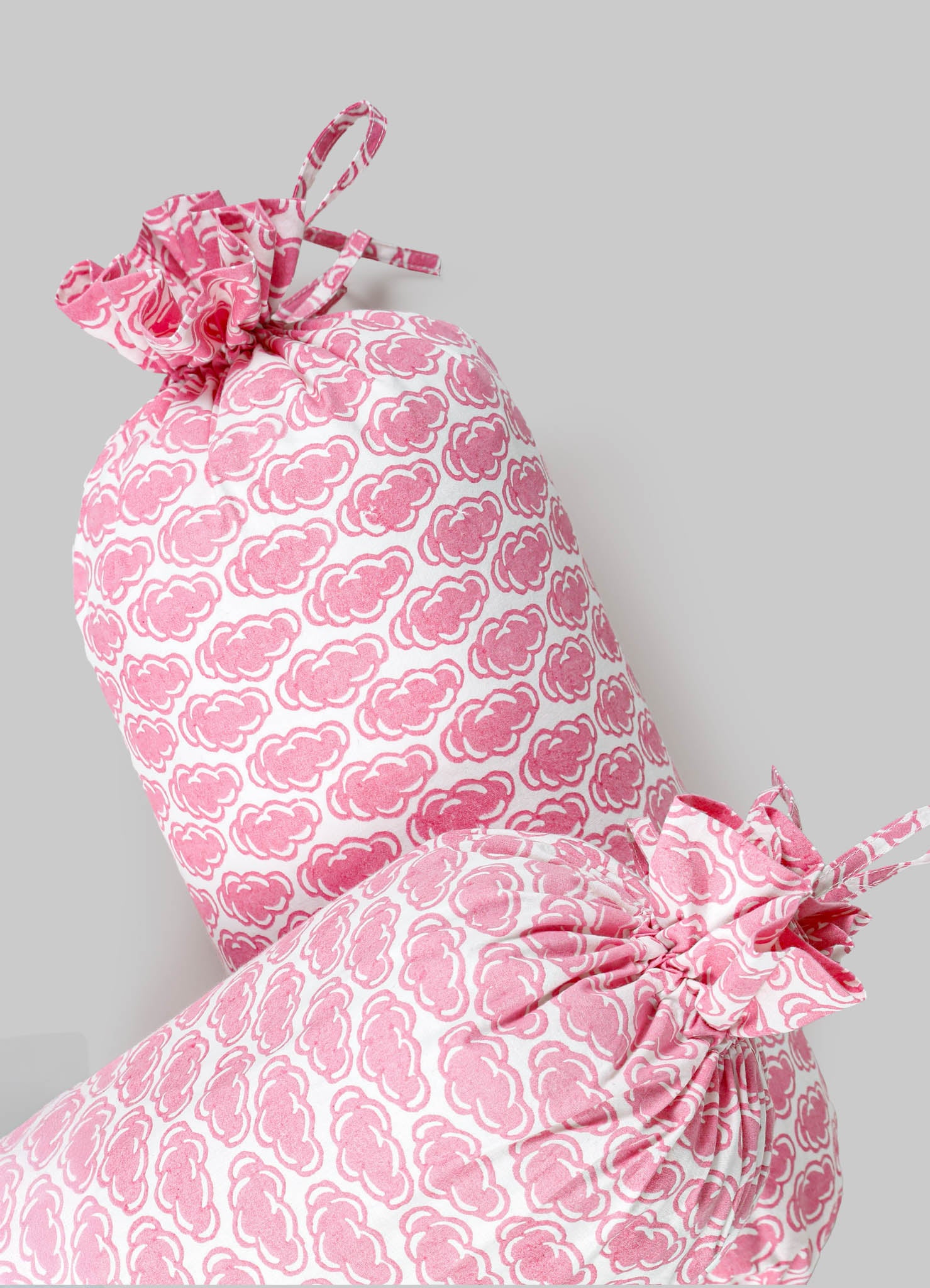 Pink and white fabric cushions with a repeating cloud-like pattern, tied at the edges with matching fabric bows, made from soft textile material.