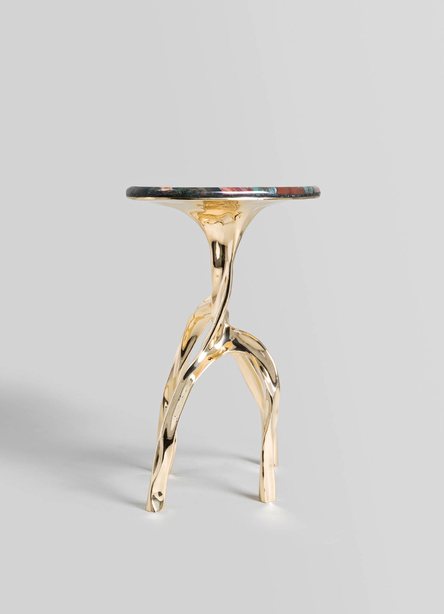 A sculptural side table with a round top made of dark marble featuring colorful veining, supported by a gold-toned metal base with organic, flowing forms resembling intertwined branches.
