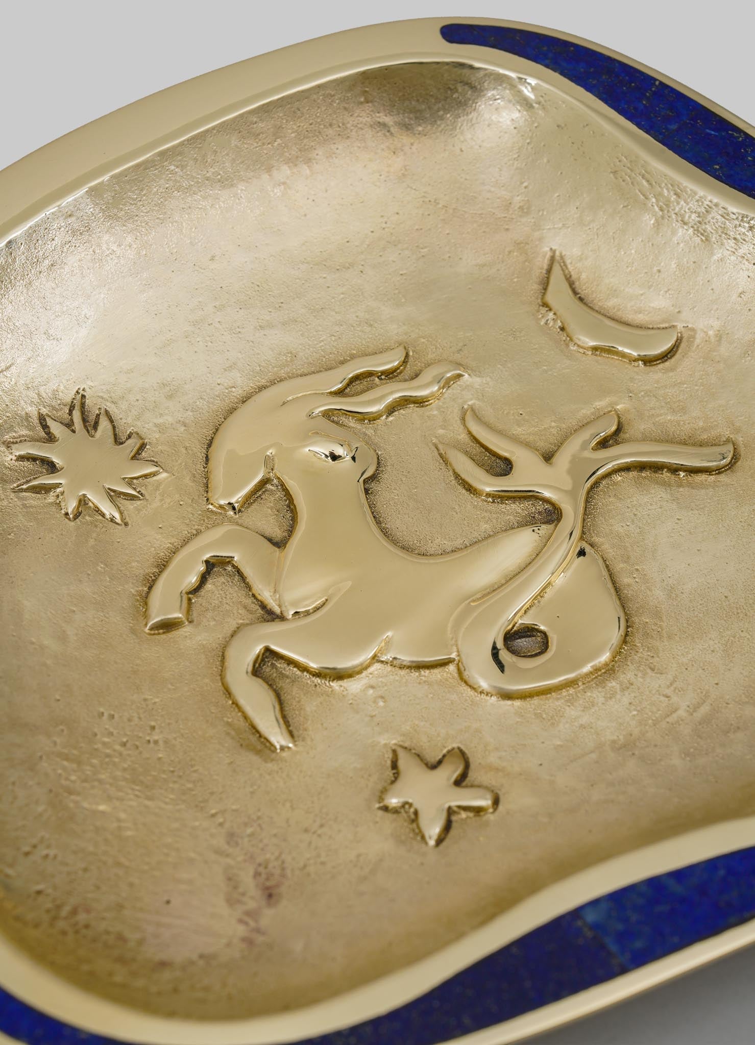 A decorative tray with a gold metallic finish featuring an embossed unicorn motif, star, and moon designs. The tray has a smooth, reflective surface with a deep blue border accents.