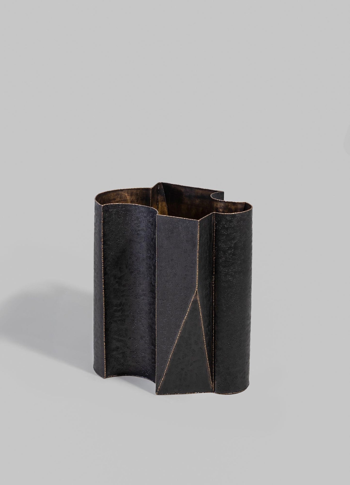 A black leather-textured vase with geometric stitching details and an angular shape, placed against a plain light gray background.