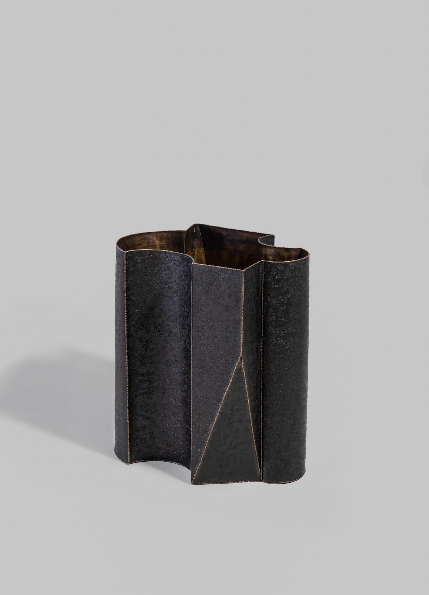 A black leather-textured vase with geometric stitching details and an angular shape, placed against a plain light gray background.