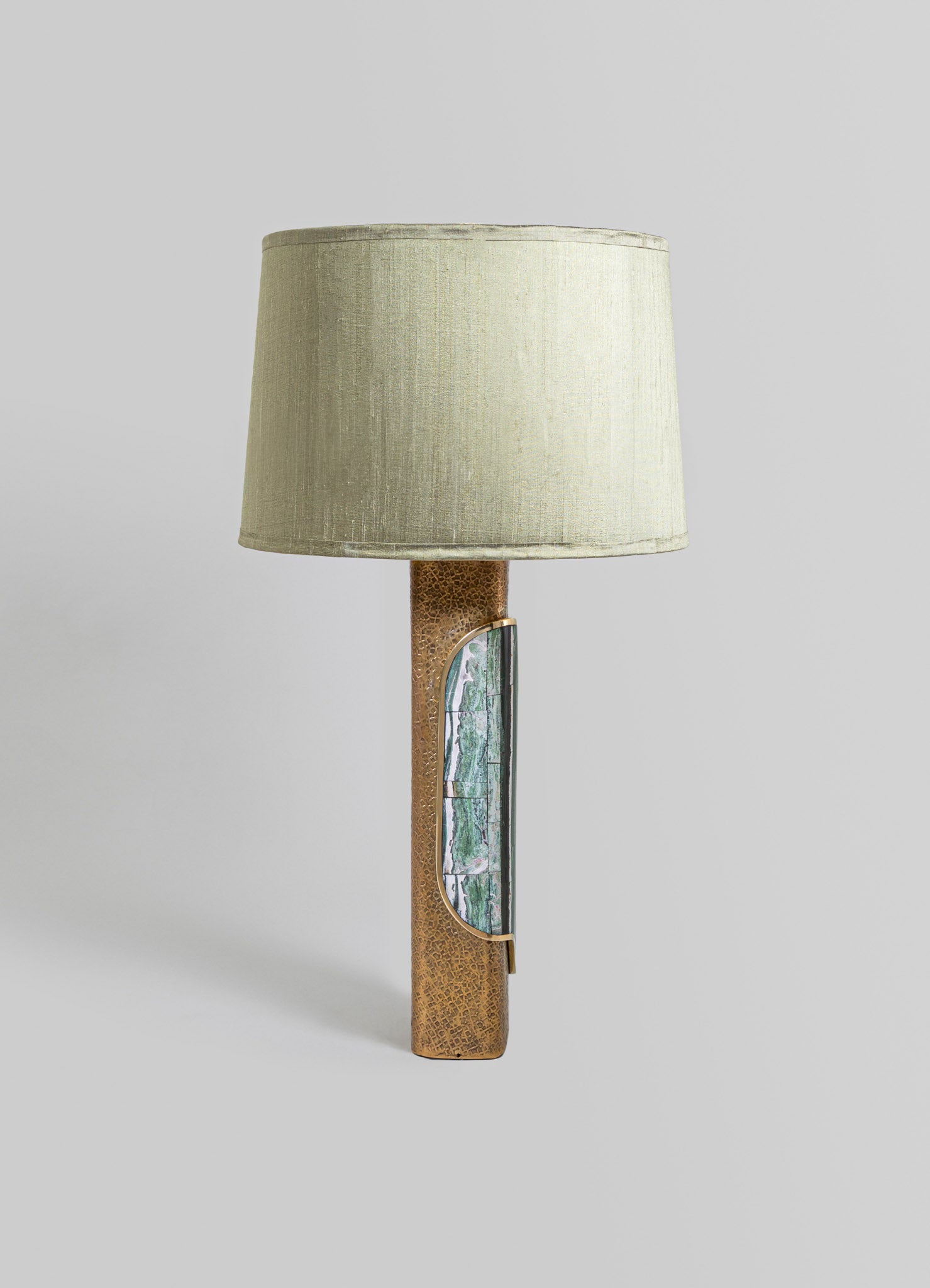 A table lamp with a cylindrical beige fabric shade and a textured brown ceramic base featuring an embedded rectangular mosaic of green, white, and purple stone.