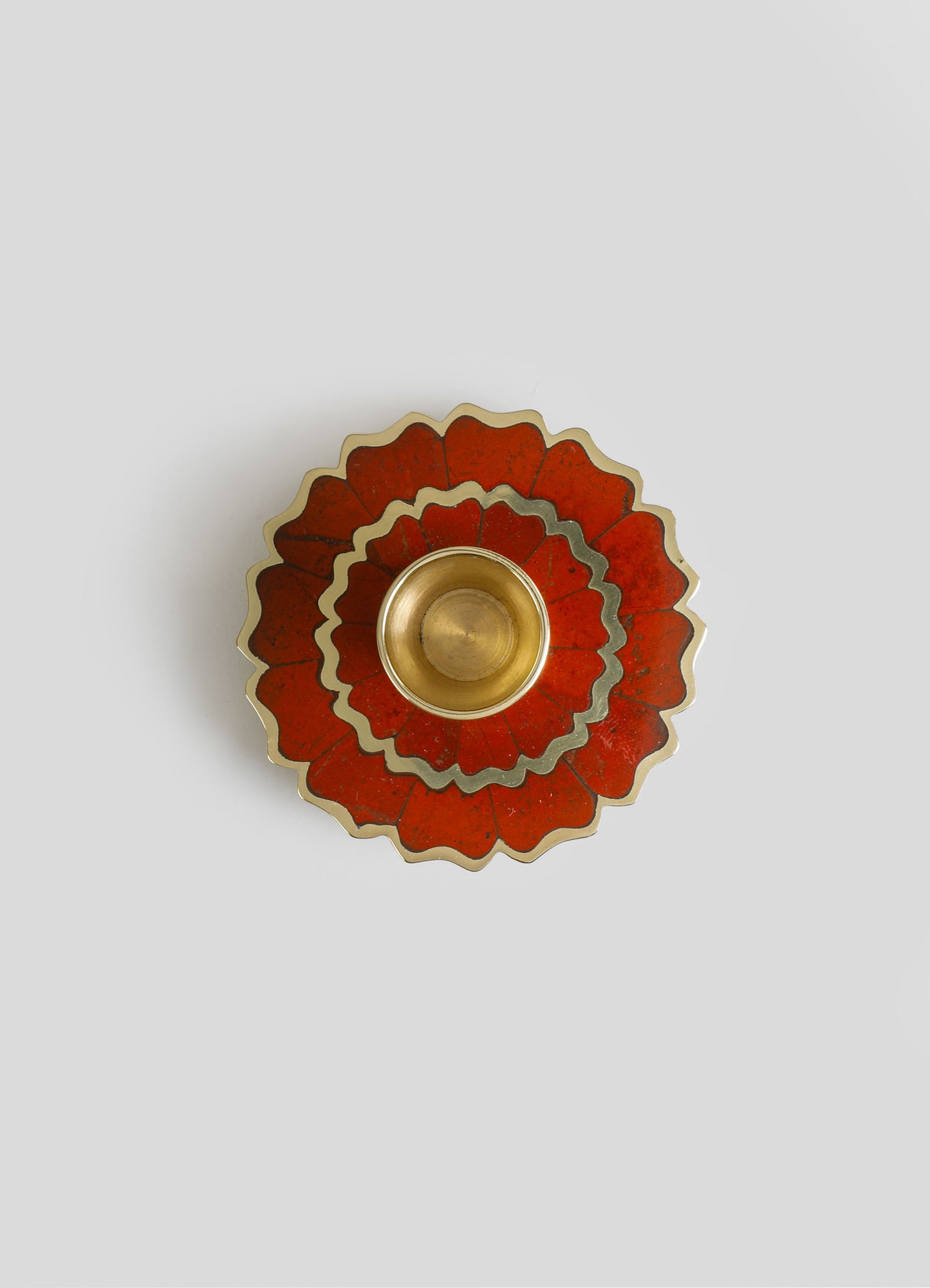 A decorative brass candle holder set with a red floral-patterned tray featuring scalloped edges and contrasting white and black accents. The set is displayed on a light gray background.