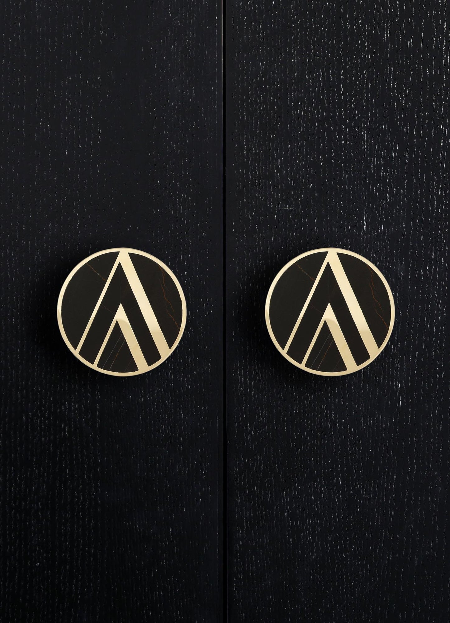 Round door handles with a black and white geometric pattern, mounted on a textured black wooden surface.