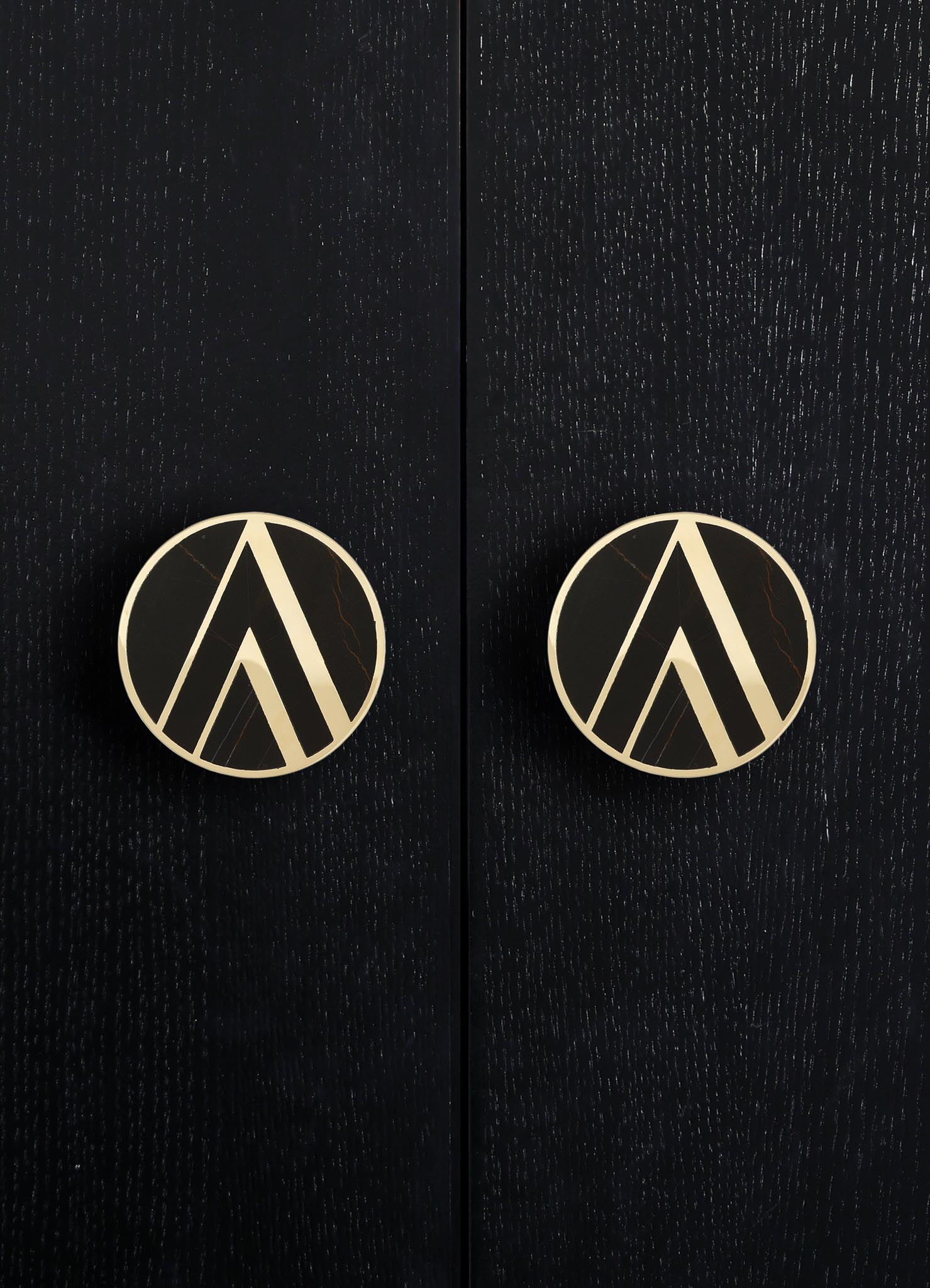 Round door handles with a black and white geometric pattern, mounted on a textured black wooden surface.