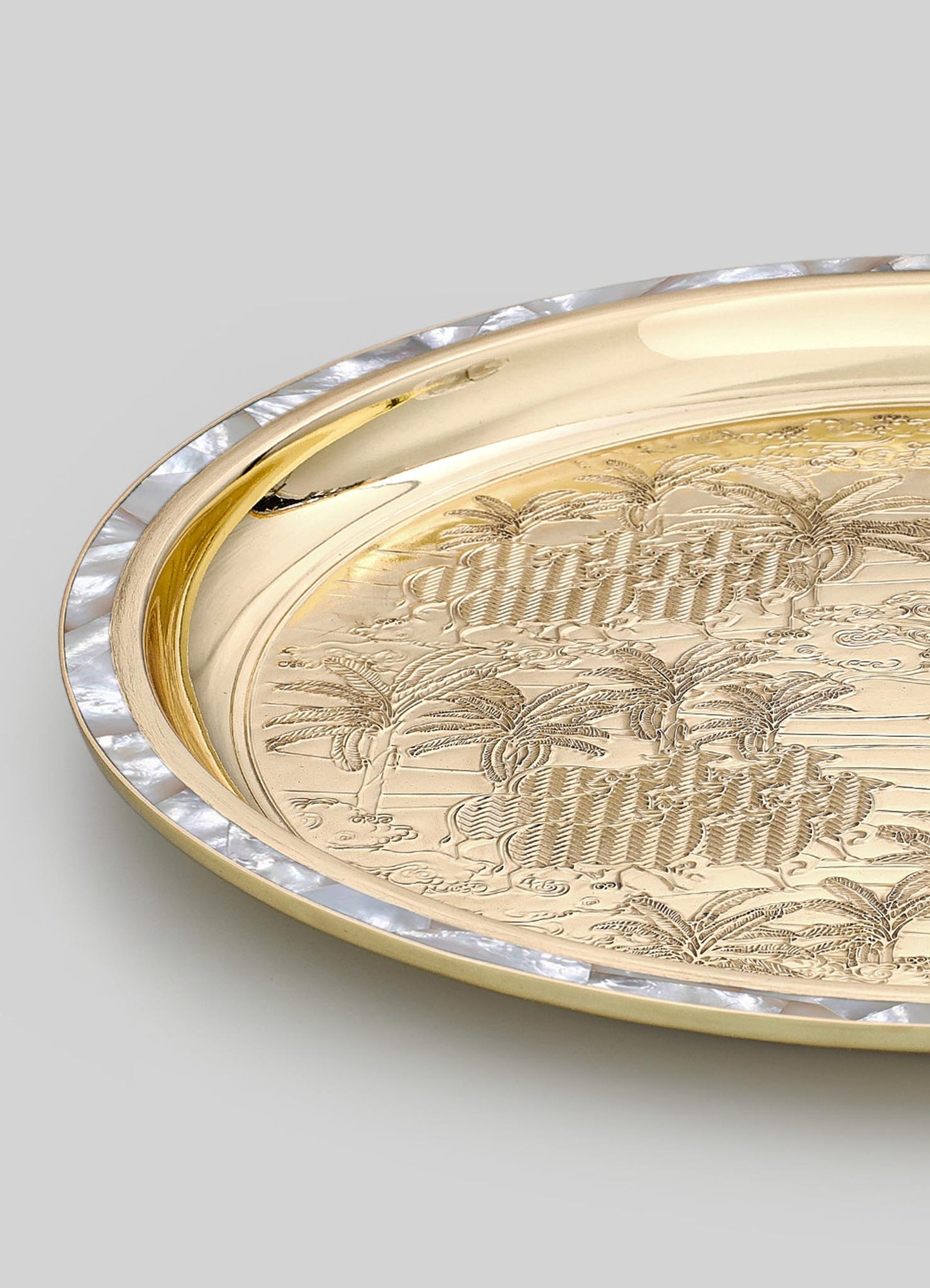 A decorative tray with a polished gold-tone surface features engraved botanical motifs and a textured pearl-like border around the edge. The tray has an elegant, vintage-inspired style with intricate detailing and a luxurious finish.