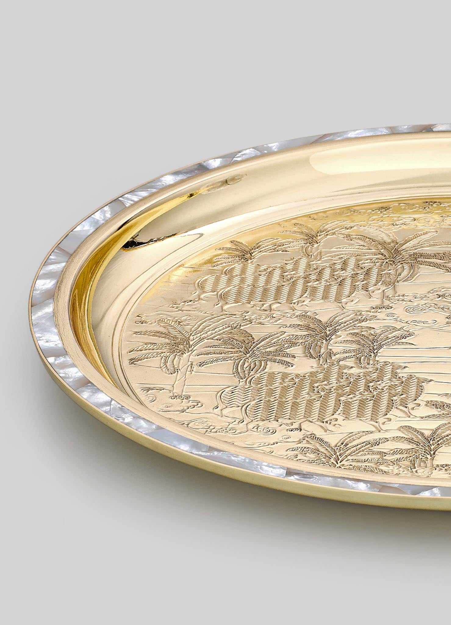A decorative tray with a polished gold-tone surface features engraved botanical motifs and a textured pearl-like border around the edge. The tray has an elegant, vintage-inspired style with intricate detailing and a luxurious finish.