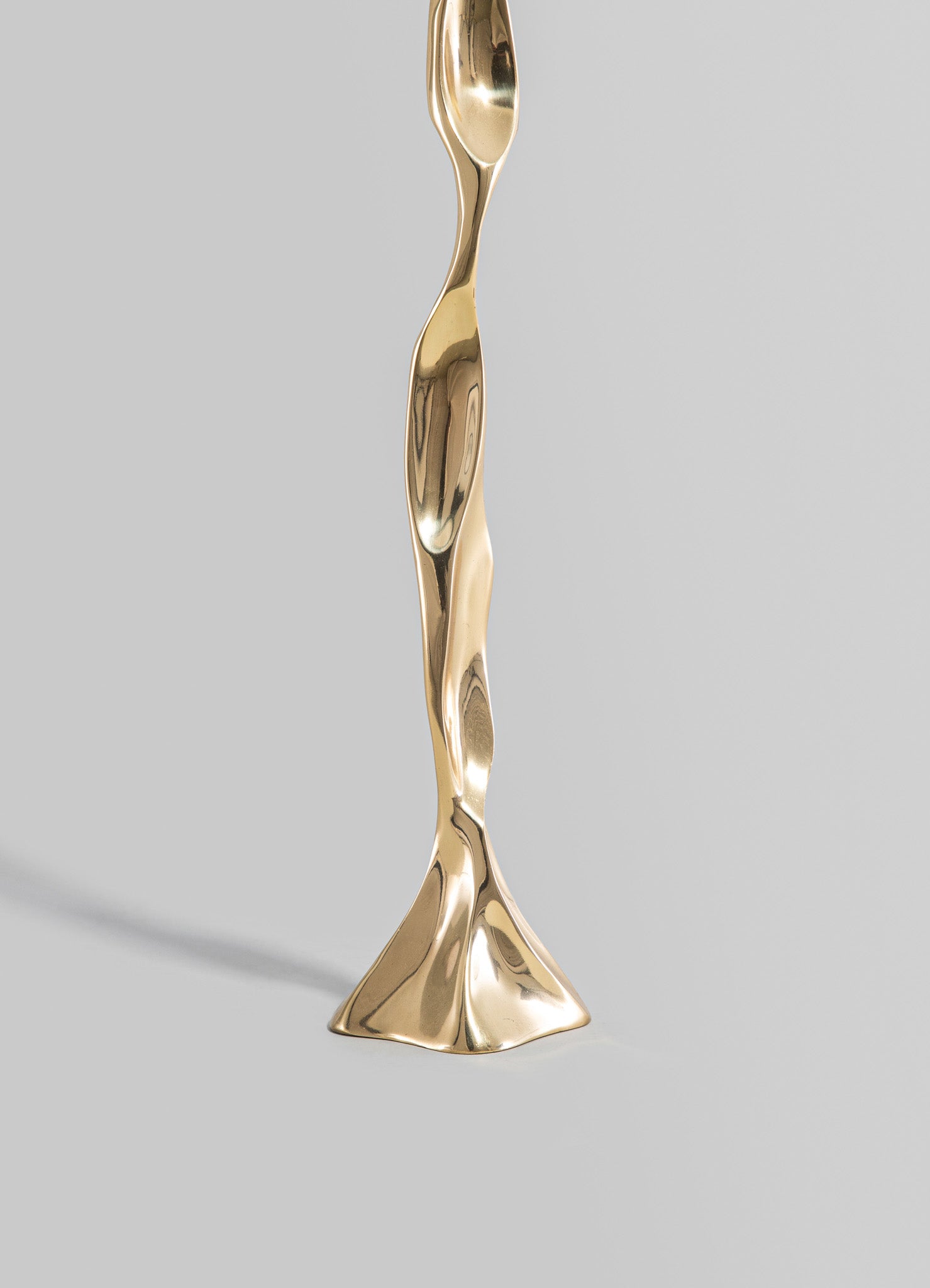 A sculptural candlestick holder made of polished brass with an abstract, flowing design, featuring a wavy, organic shape and a reflective surface.
