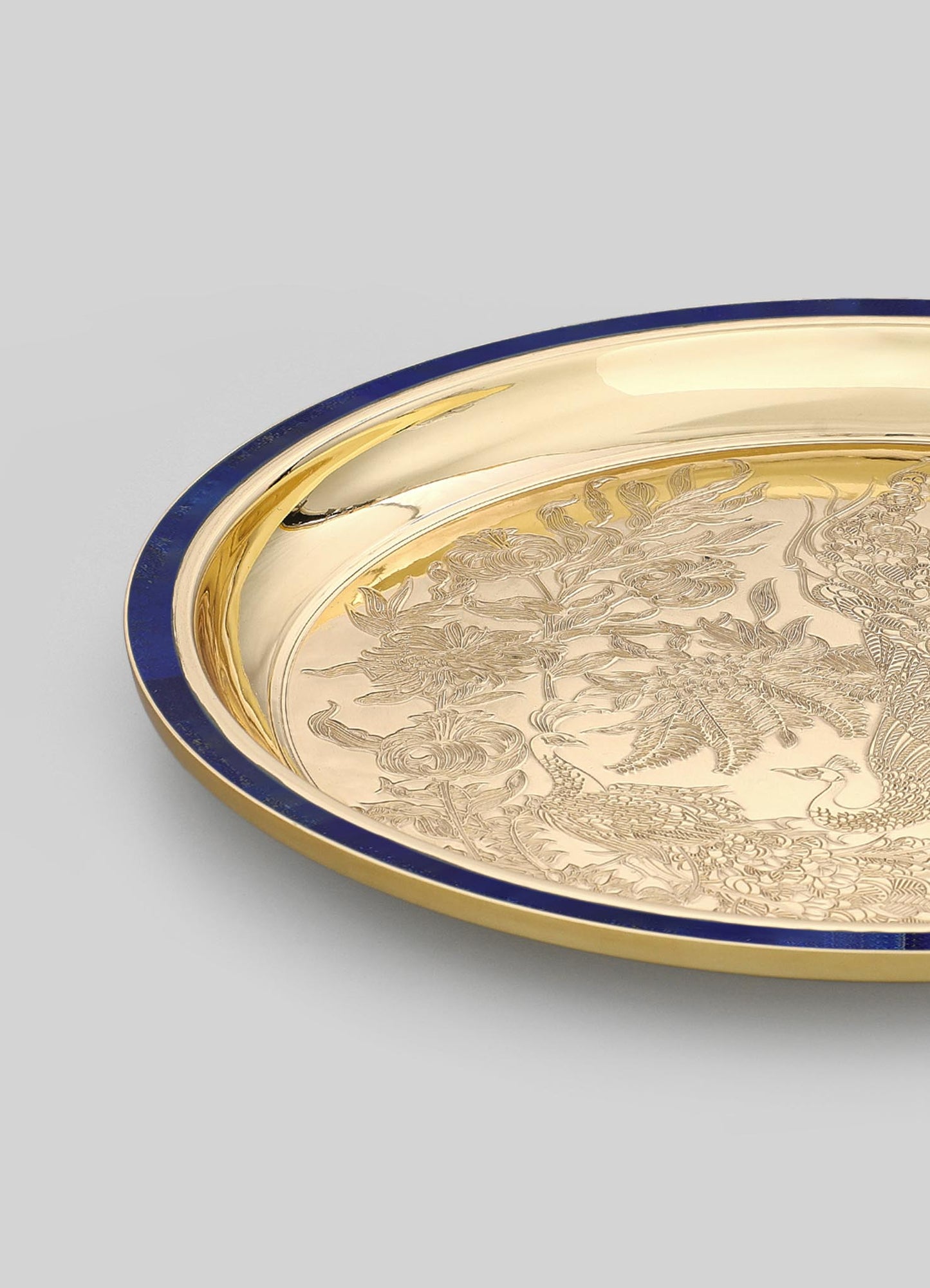 A decorative tray made of polished brass with an engraved floral and bird motif, featuring a deep blue border around the edge, set against a neutral background.