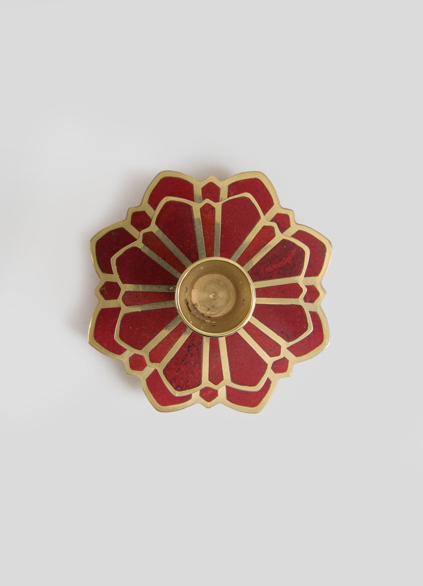 A decorative candle holder with a flower-shaped design featuring red and gold materials, with a central cavity for a candle. The piece has a handcrafted appearance with bold, contrasting colors.