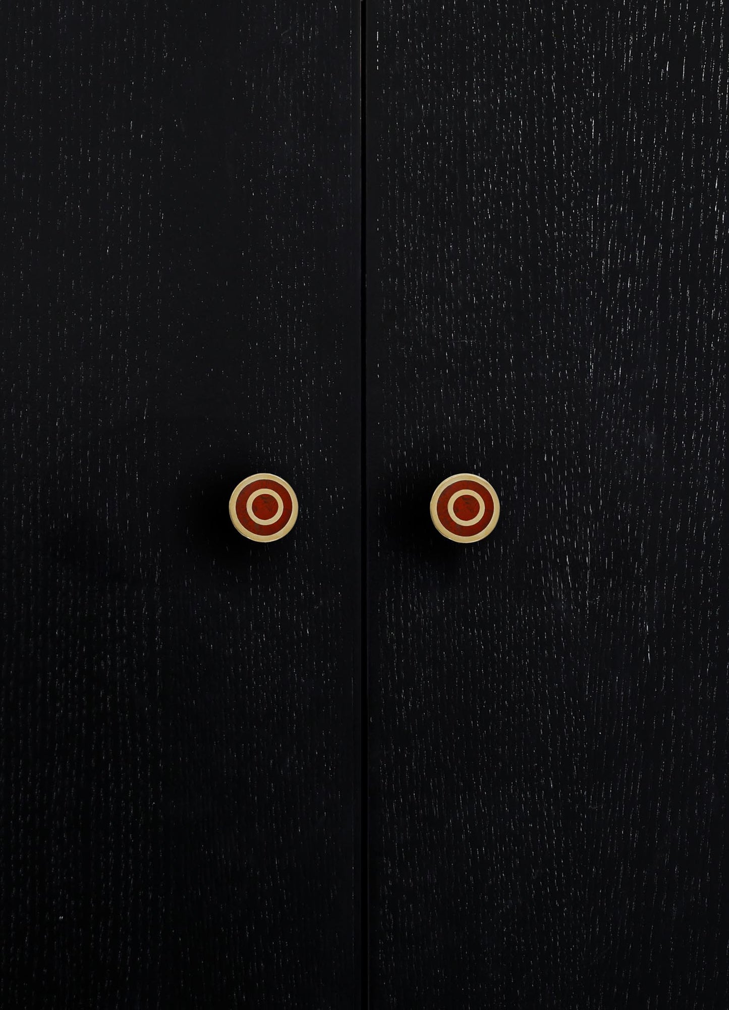 Close-up of black wooden cabinet doors with a textured finish and round brass knobs with red circular accents.