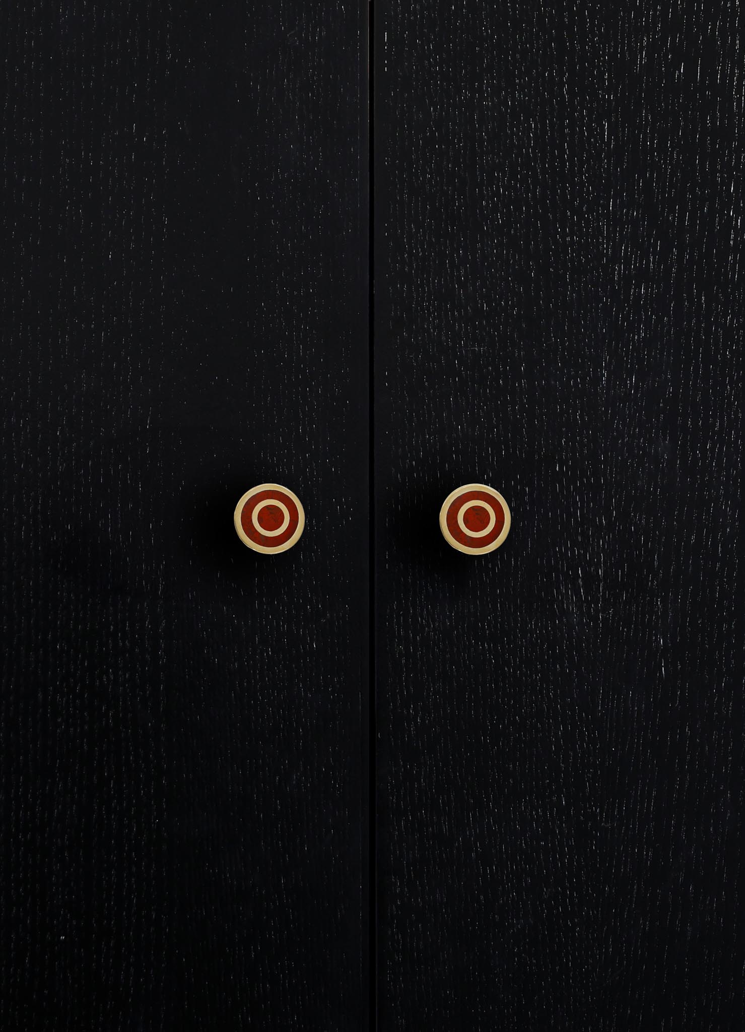 Close-up of black wooden cabinet doors with a textured finish and round brass knobs with red circular accents.