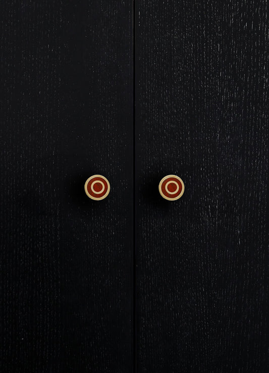 Close-up of black wooden cabinet doors with a textured finish and round brass knobs with red circular accents.