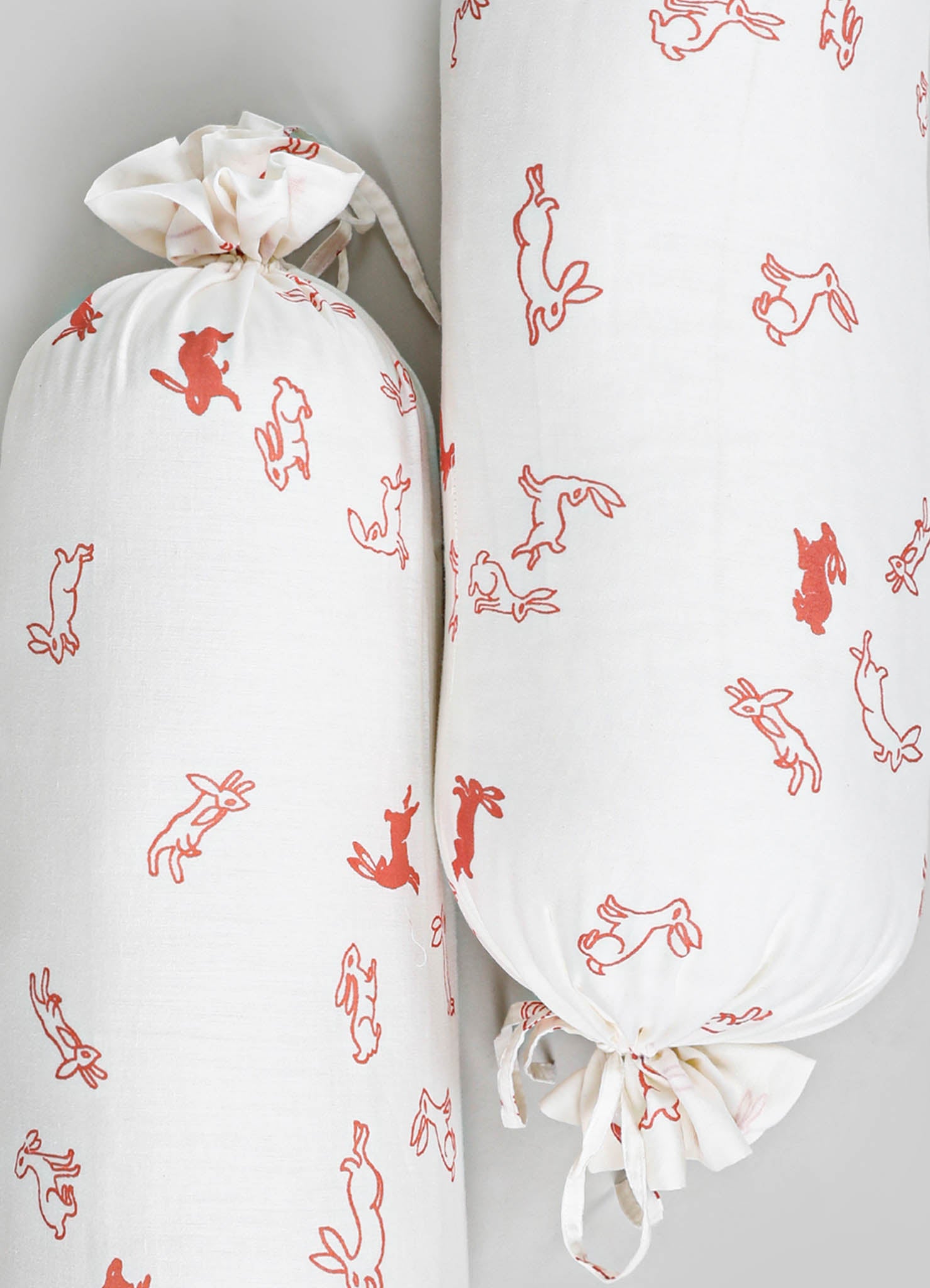 White fabric storage bag and roller with printed red bunny and hare motifs, made of lightweight cotton or linen material, with a casual, playful style.