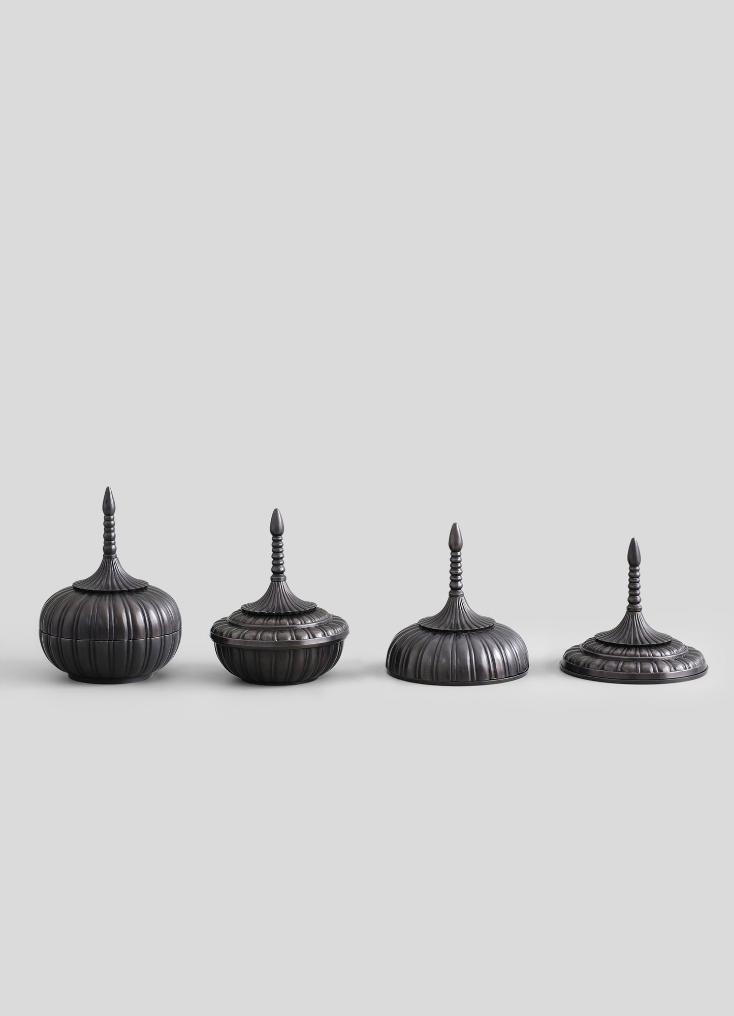 Set of four antique-style finials or decorative ornaments made of dark metal with vertical ribbing and pointed tops, featuring intricate spindle-shaped details on the slender, elongated finials.
