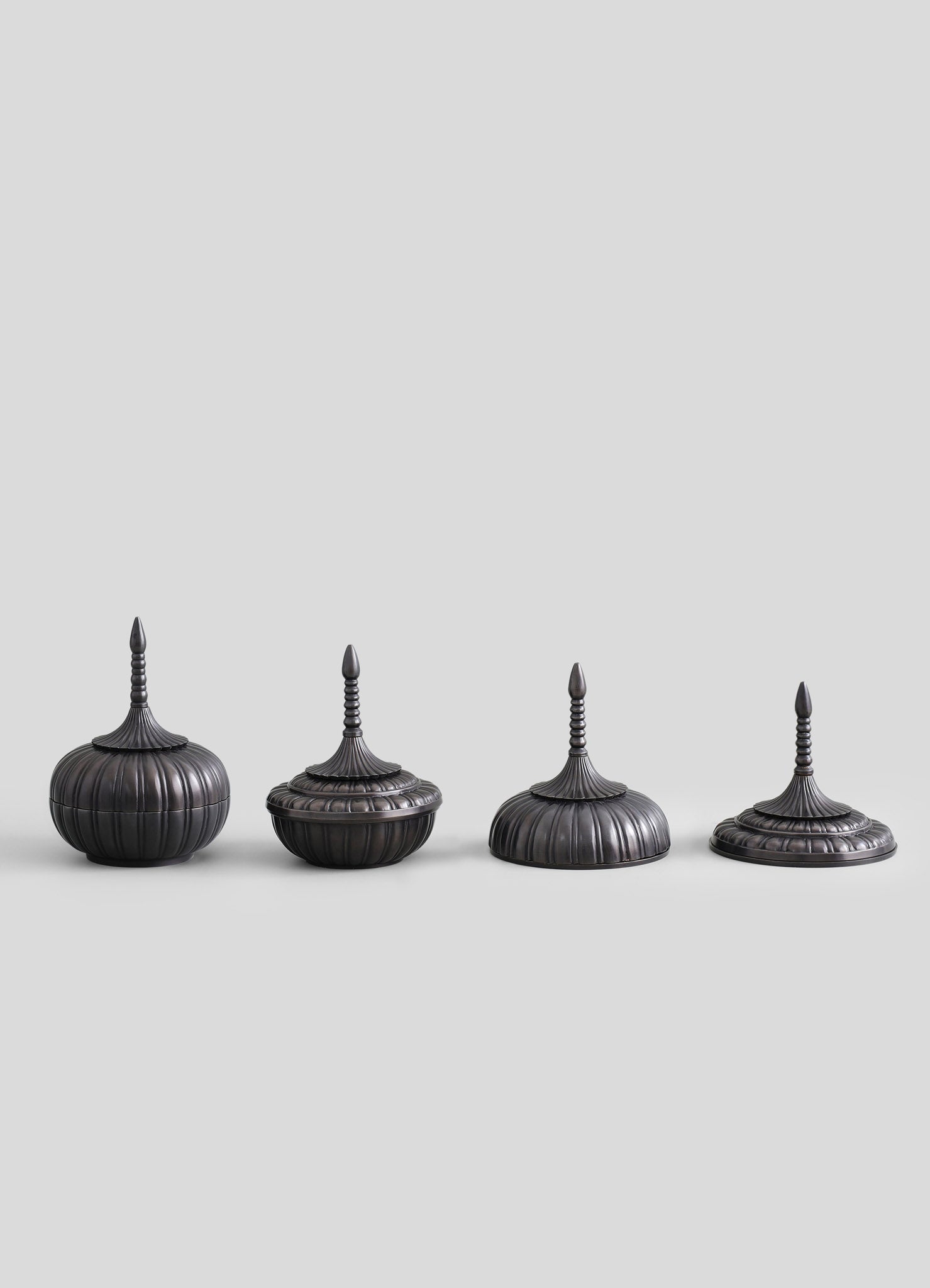 Set of four antique-style finials or decorative ornaments made of dark metal with vertical ribbing and pointed tops, featuring intricate spindle-shaped details on the slender, elongated finials.