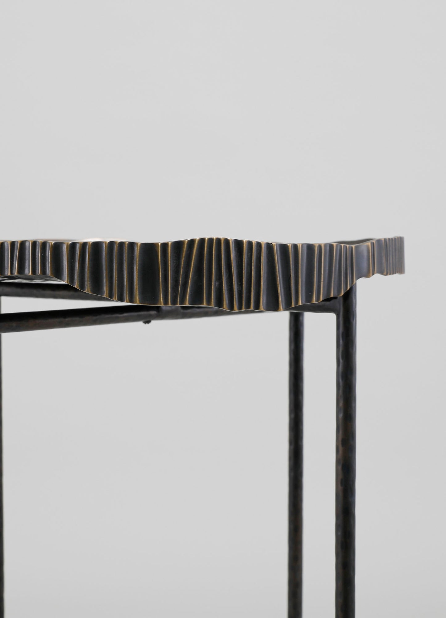 A metal table with a textured, wavy edge in a dark finish with subtle gold accents, supported by slender black legs, in a minimalist style.