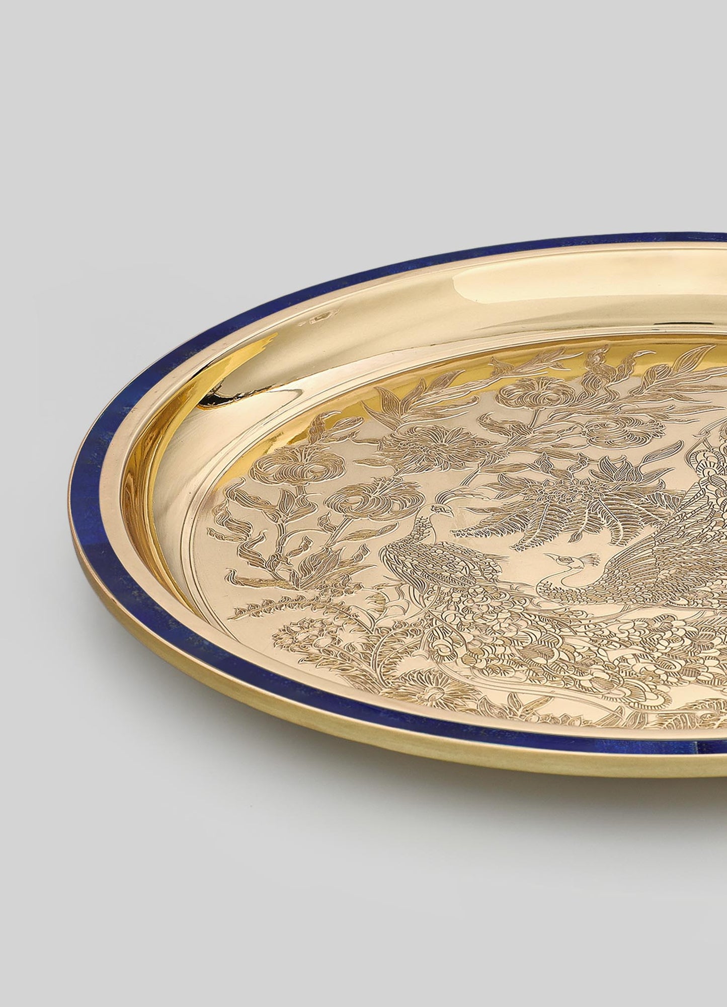 Decorative round tray with a gold finish and a dark blue rim, featuring intricate engraved motifs of birds, flowers, and foliage. The design combines traditional craftsmanship with a luxurious and elegant style.