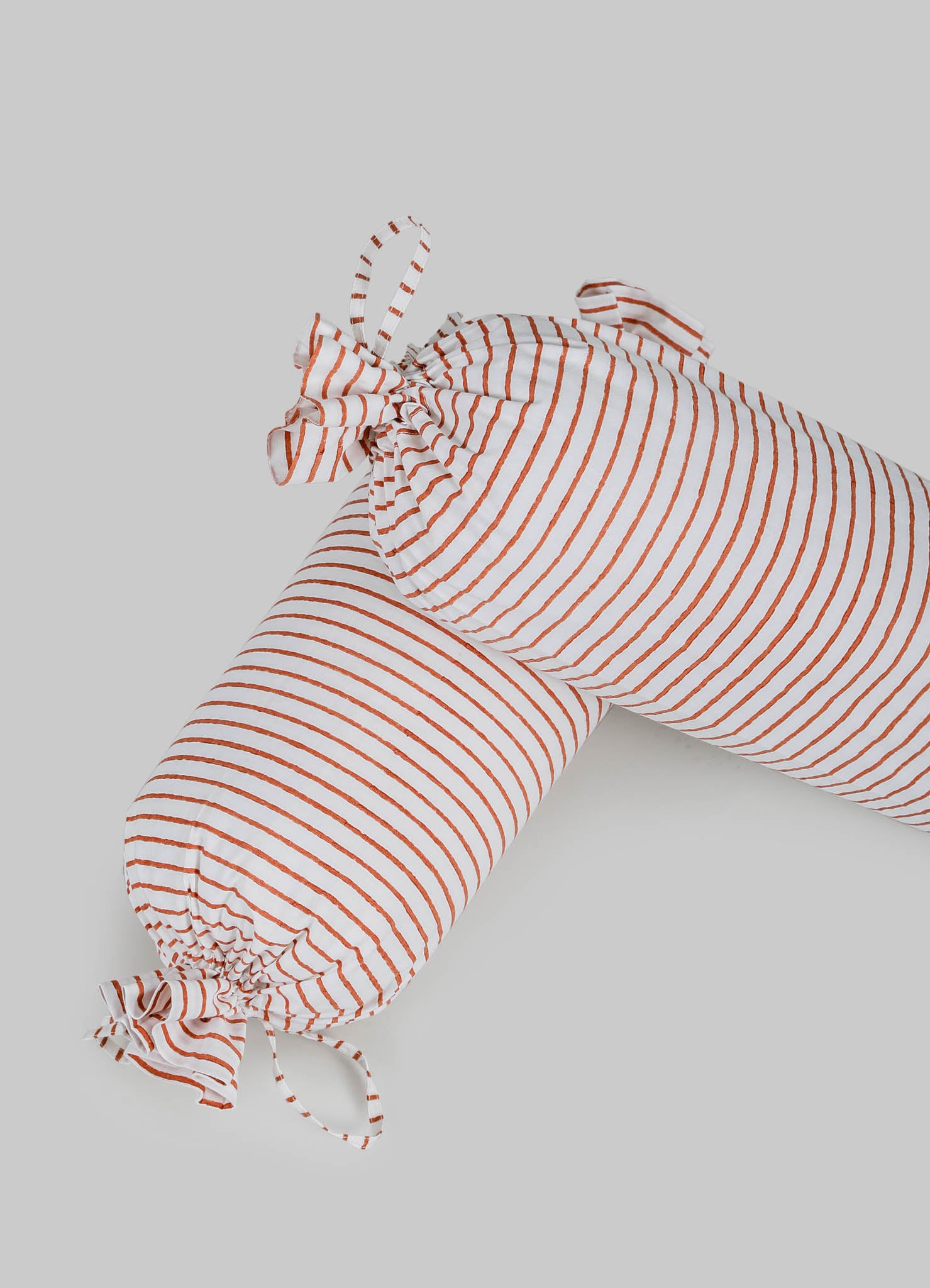 A striped fabric item, likely a cushion cover or textile, made from lightweight material with white and rust-red horizontal lines. It features fabric ties at the corners, creating a gathered effect, in a casual or contemporary style.