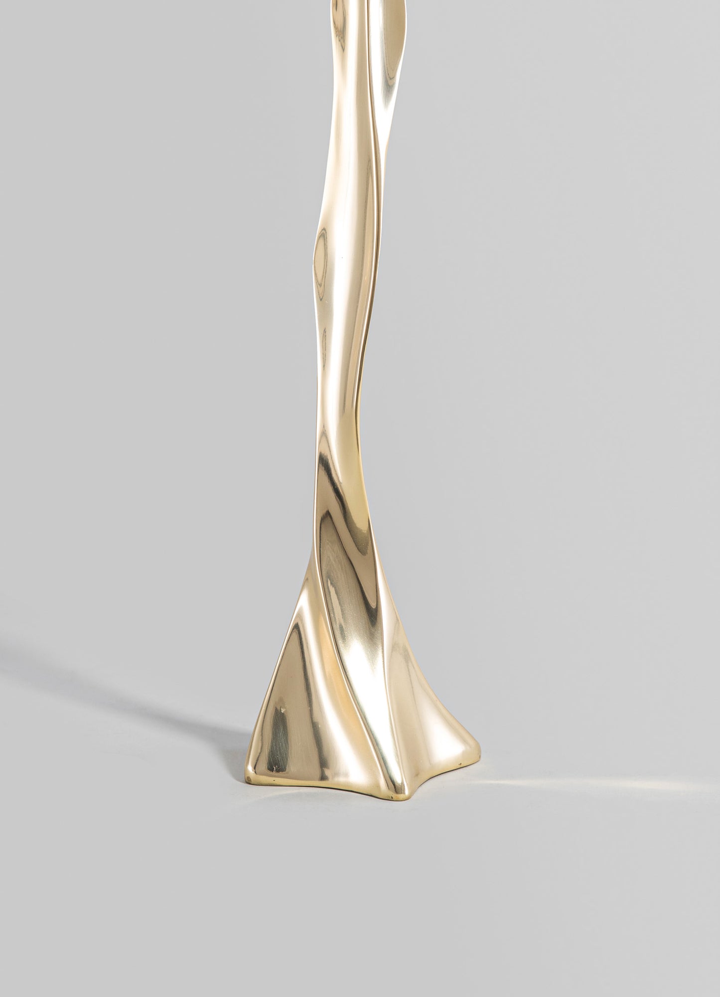 A gold-colored metal sculpture with a twisted, abstract form and smooth, reflective surface, set against a neutral background.