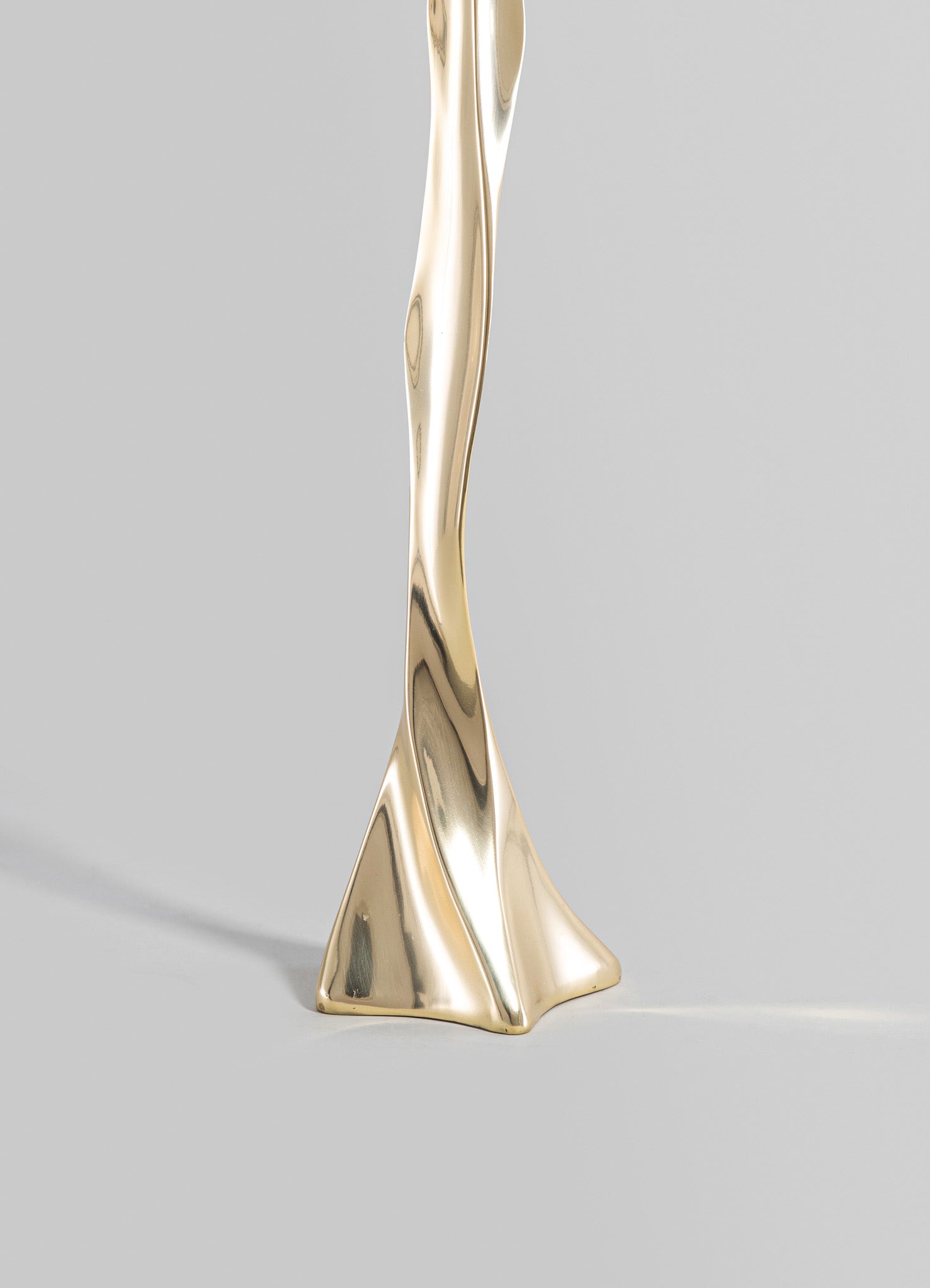 A gold-colored metal sculpture with a twisted, abstract form and smooth, reflective surface, set against a neutral background.