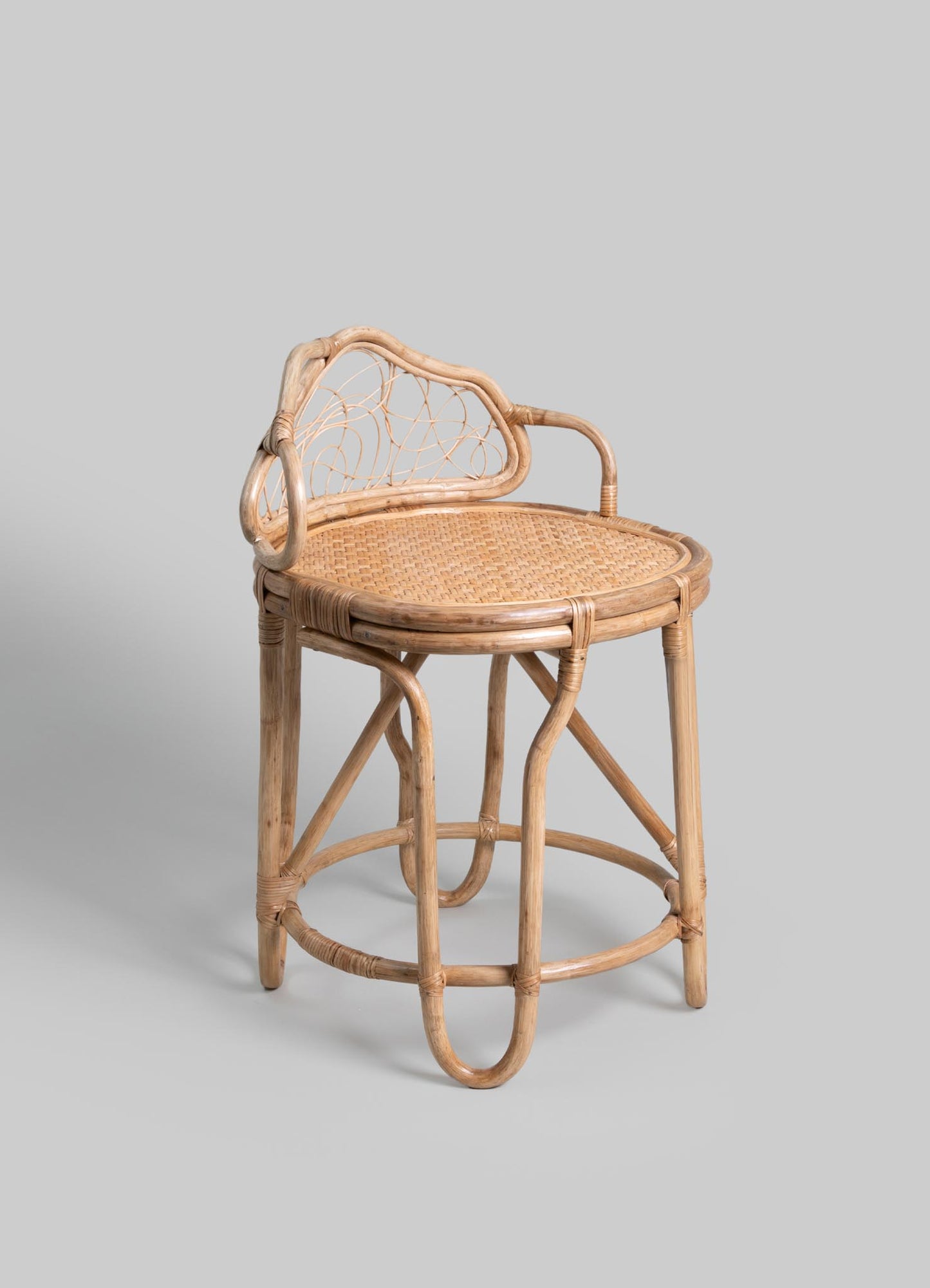 A rattan accent chair with a woven cane seat and a decorative openwork backrest, featuring curved armrests and a circular base. The natural wood finish and handcrafted design evoke a rustic, bohemian style.