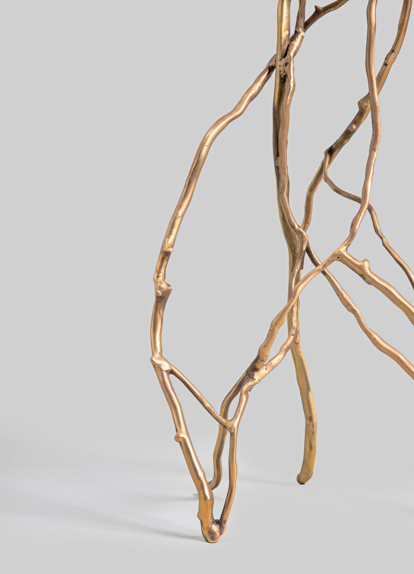 A decorative metal sculpture featuring elongated, twisted branches with a polished gold finish, set against a neutral background.