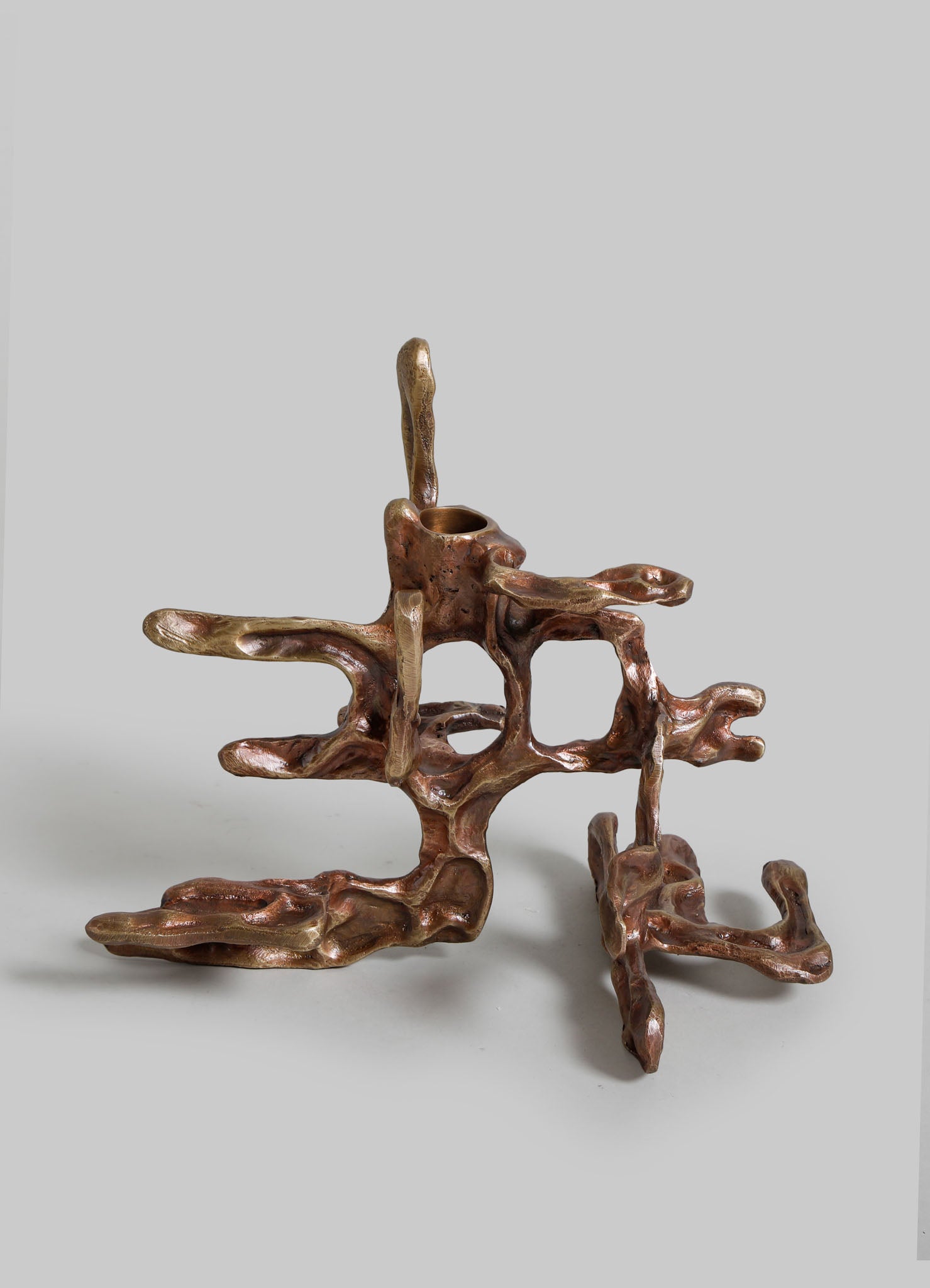 A sculptural object resembling intertwined branches or driftwood with a polished, reddish-brown finish, featuring an irregular, organic form. The piece has a hollow central section and a tall, slender protrusion extending upward from it.