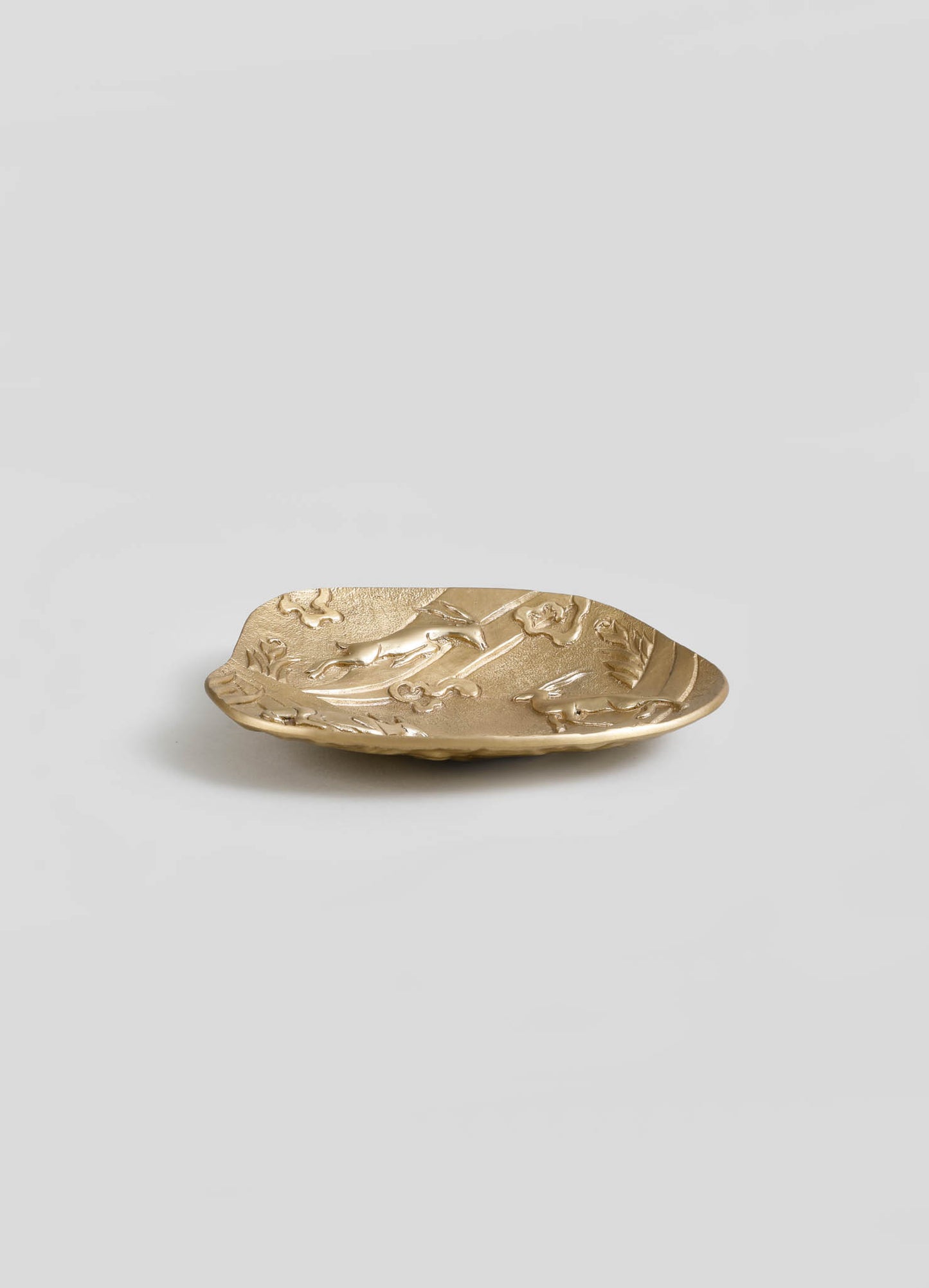 A brass dish with an embossed floral motif, featuring a curved, irregular shape and a shiny, gold-toned finish.