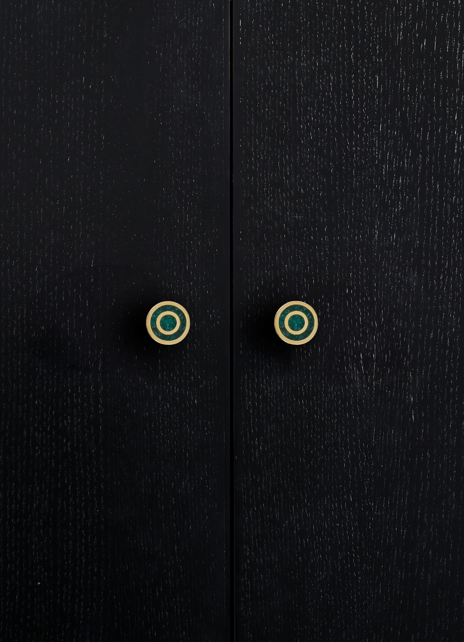Black wooden cabinet with a textured finish and round, gold-accented drawer handles featuring concentric circles. The design is contemporary with a focus on sleek, minimalist aesthetics.