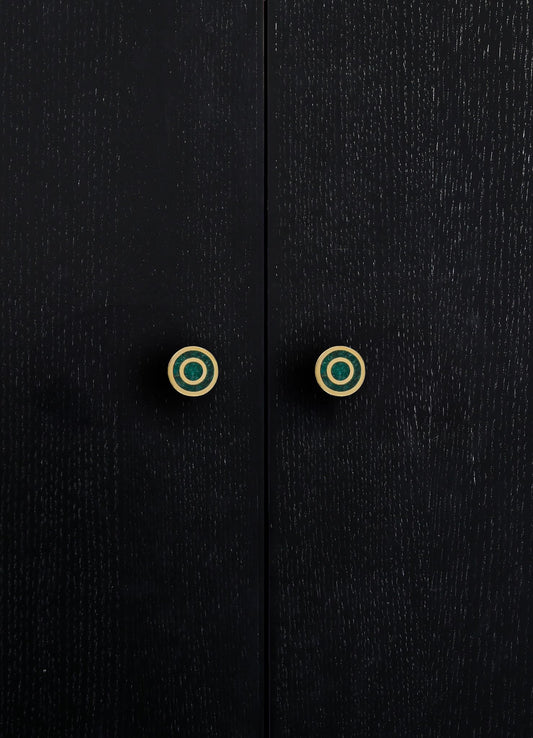 Black wooden cabinet with a textured finish and round, gold-accented drawer handles featuring concentric circles. The design is contemporary with a focus on sleek, minimalist aesthetics.