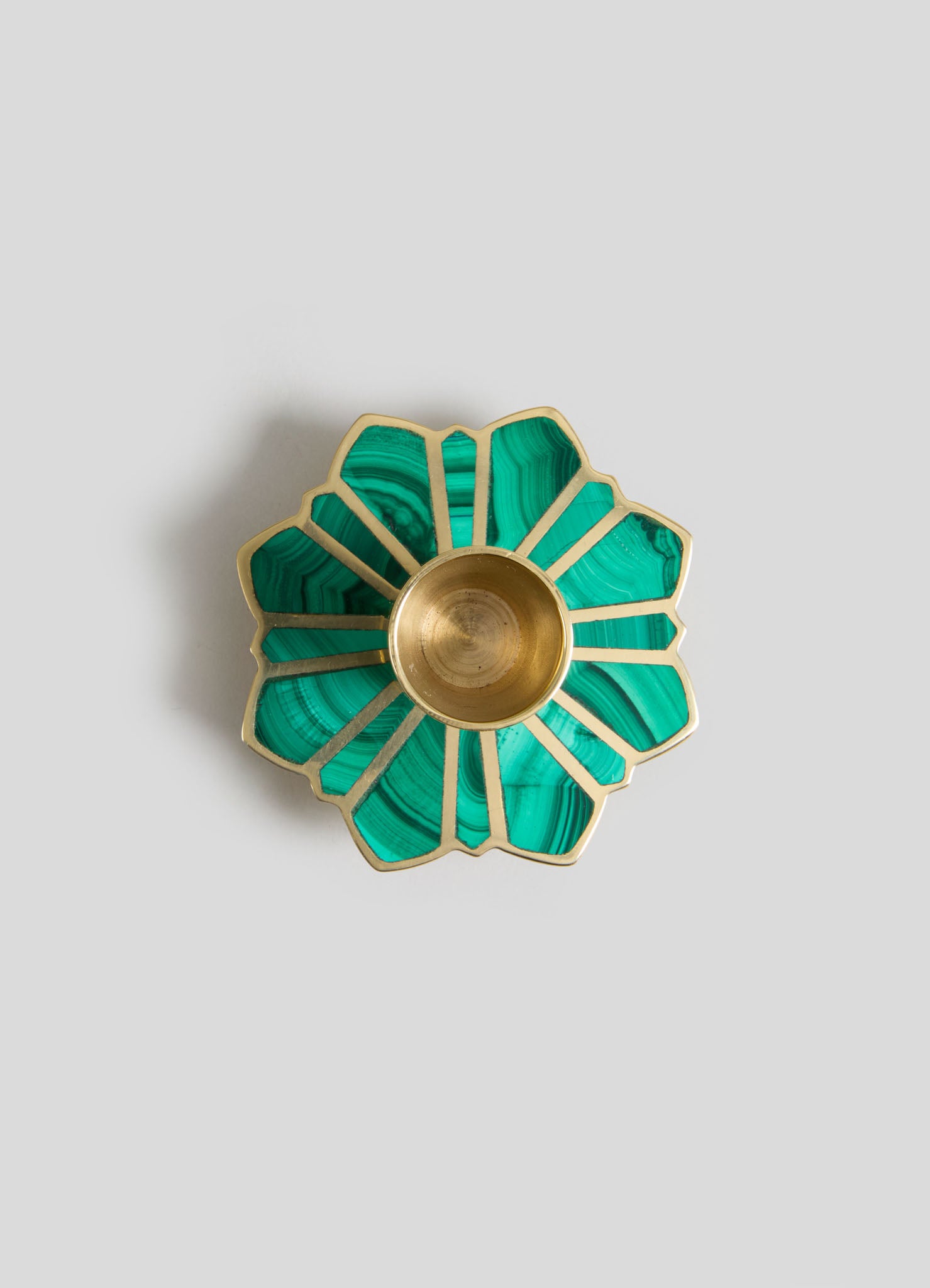 A decorative bowl with a flower petal shape, featuring green malachite inlays and gold metal accents, with a smooth circular interior at the center.
