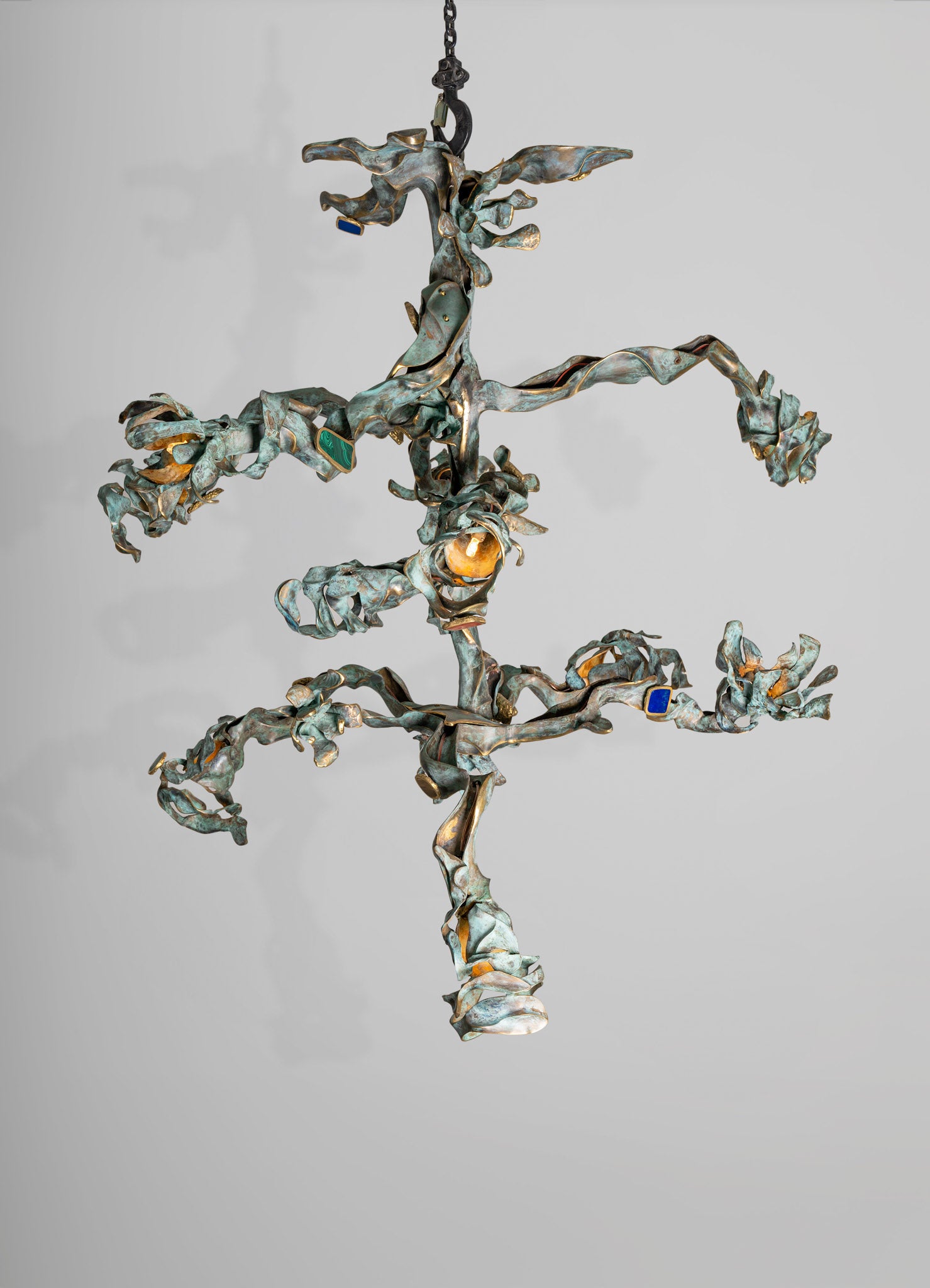 Metallic wall sconce with an abstract, sculptural design featuring twisted, leaf-like shapes in a weathered bronze finish, with small blue and green inlays.