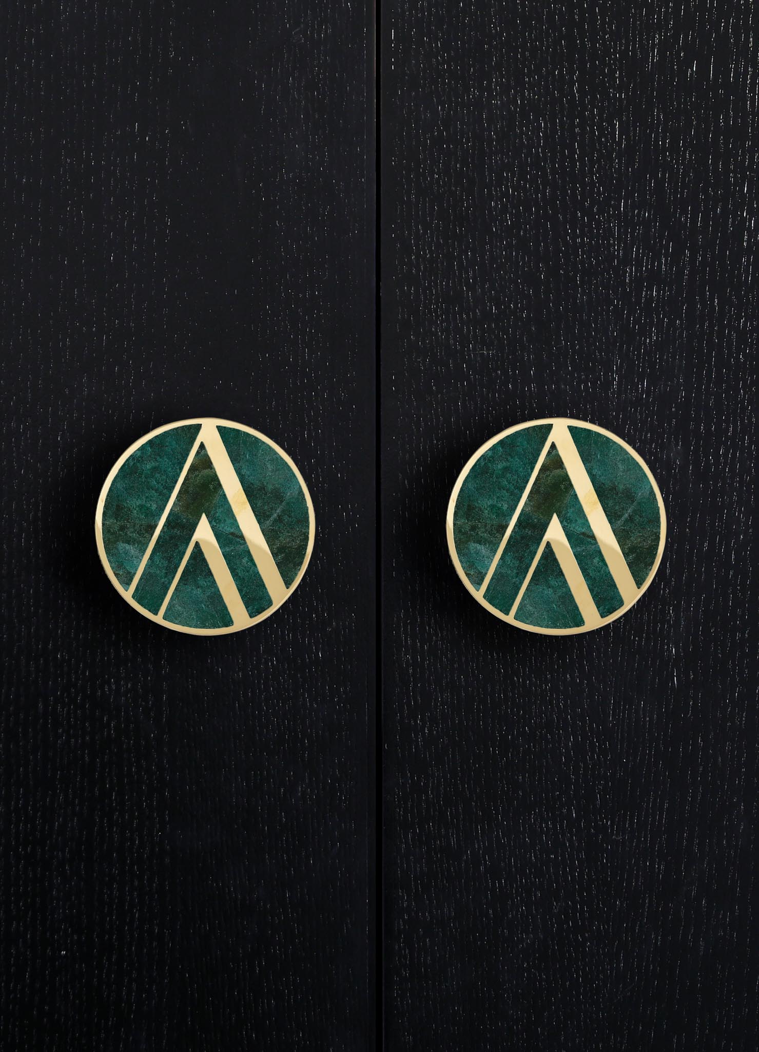 Round earrings featuring a geometric pattern with gold outlines and a green and blue marbled interior, set against a dark, textured background.