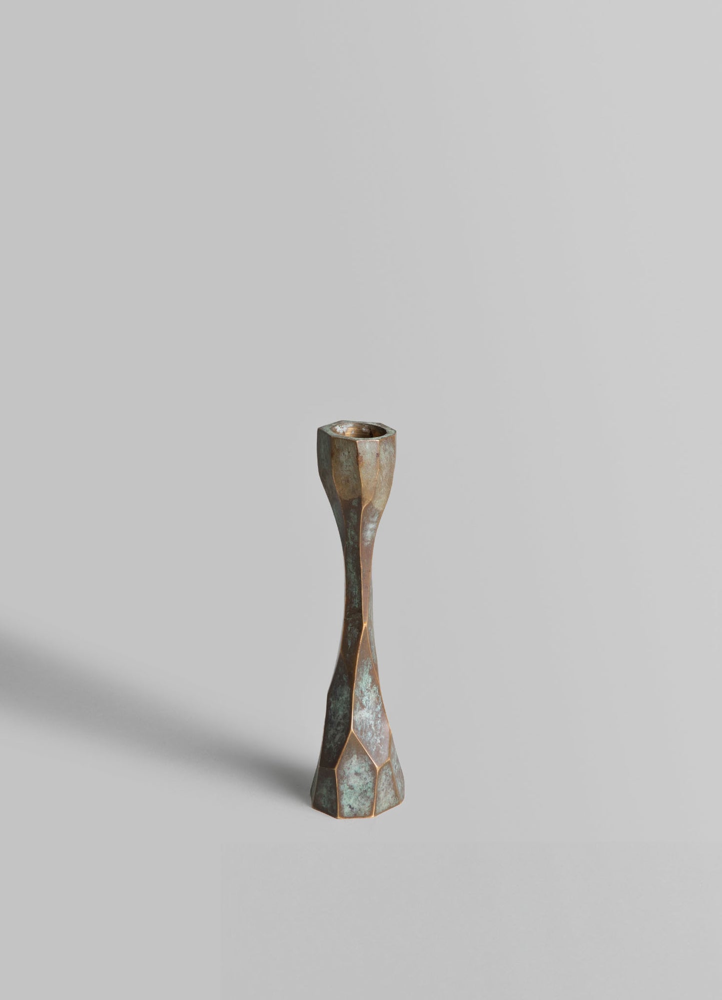A tall, geometric metal candle holder with a distressed finish, featuring an elongated hourglass shape and a hexagonal-patterned base.