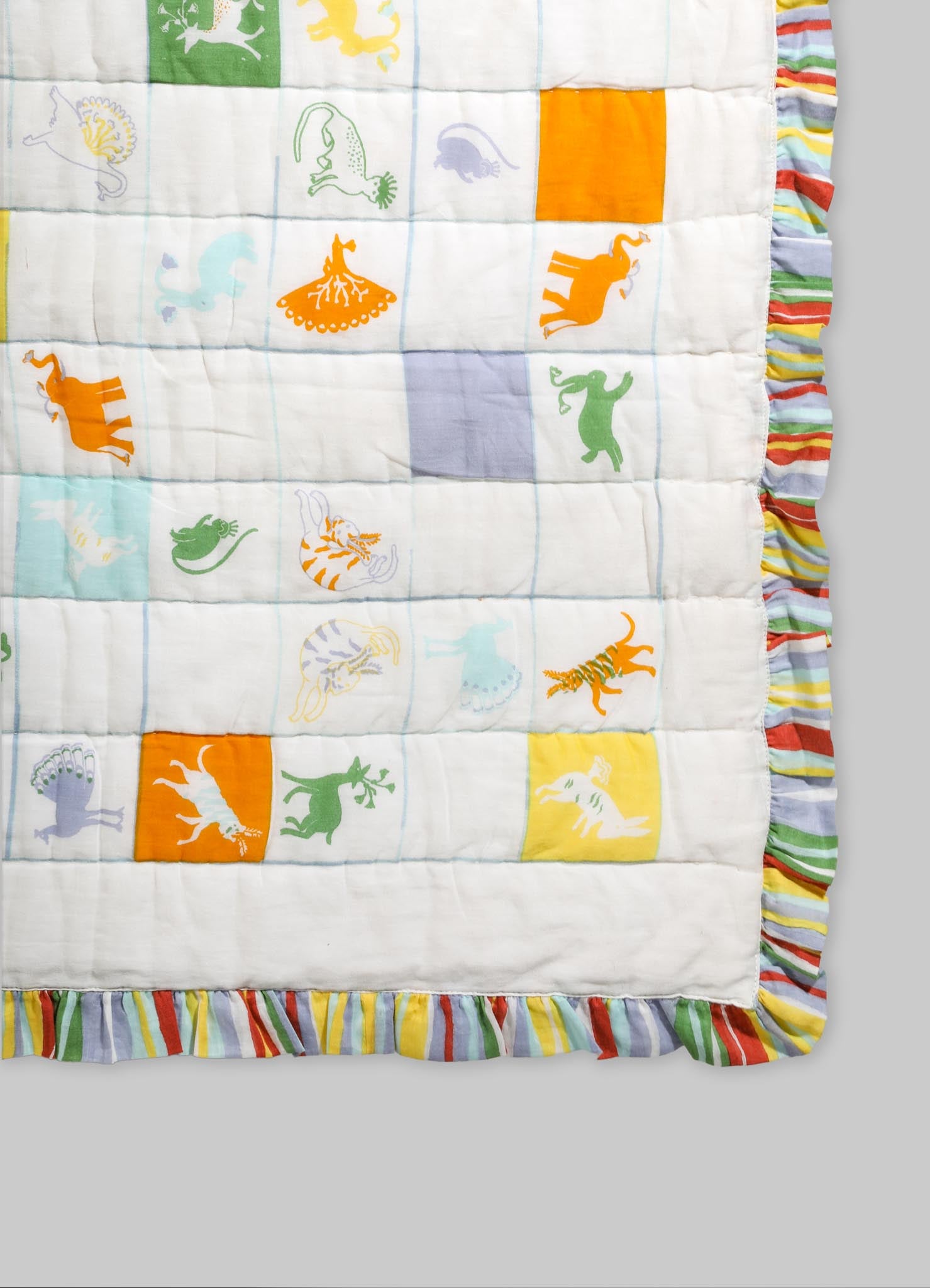 Cotton quilt with colorful animal motifs including lions, zebras, and elephants arranged in a patchwork design, bordered with striped ruffle in red, yellow, green, blue, and white.