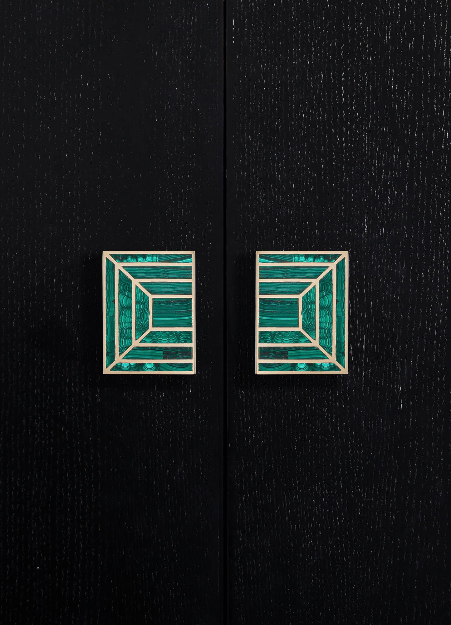 Decorative cabinet handles featuring square brass bases with intricate geometric patterns filled with teal malachite inlays, mounted on a black wooden surface.