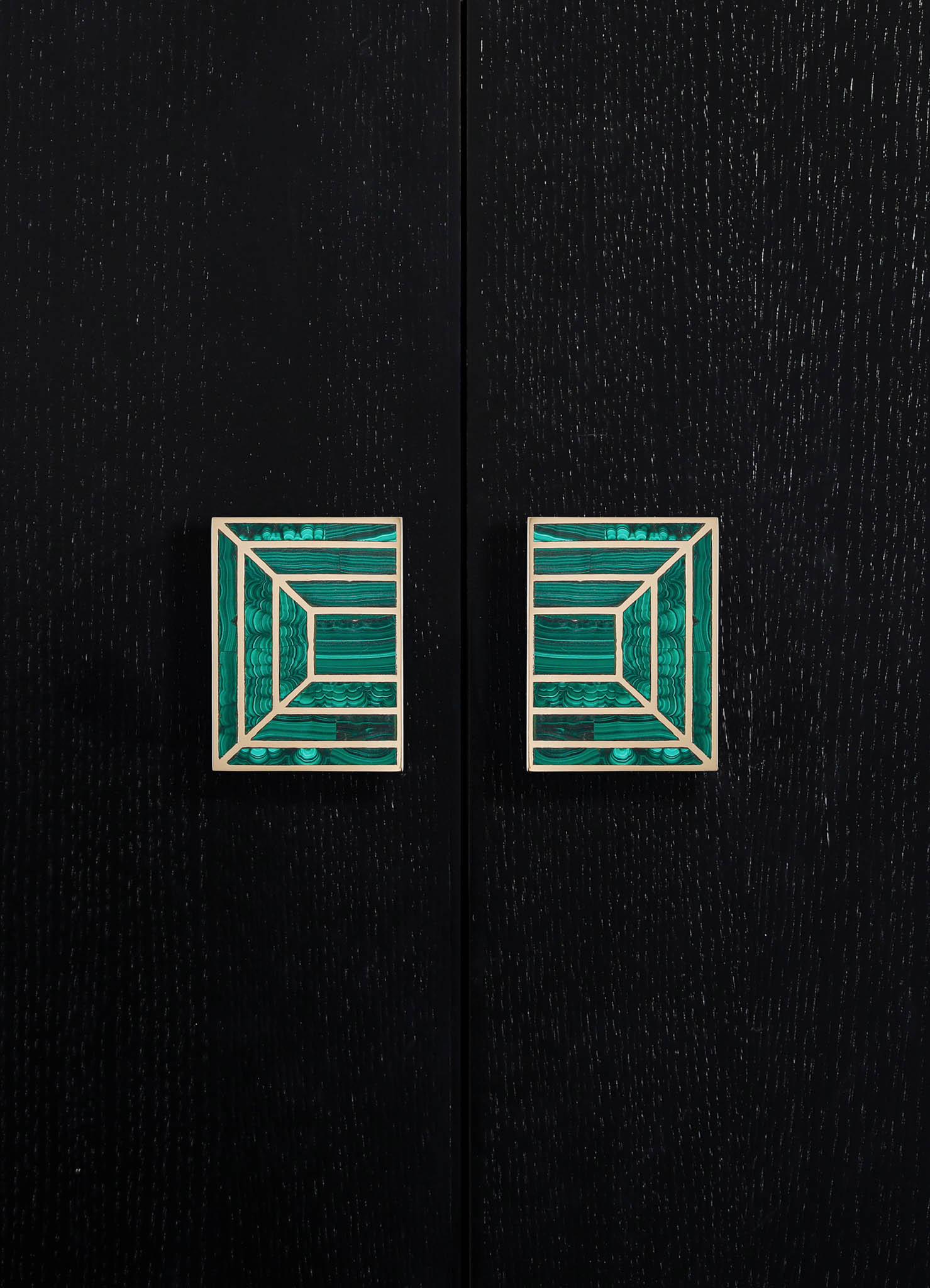 Decorative cabinet handles featuring square brass bases with intricate geometric patterns filled with teal malachite inlays, mounted on a black wooden surface.