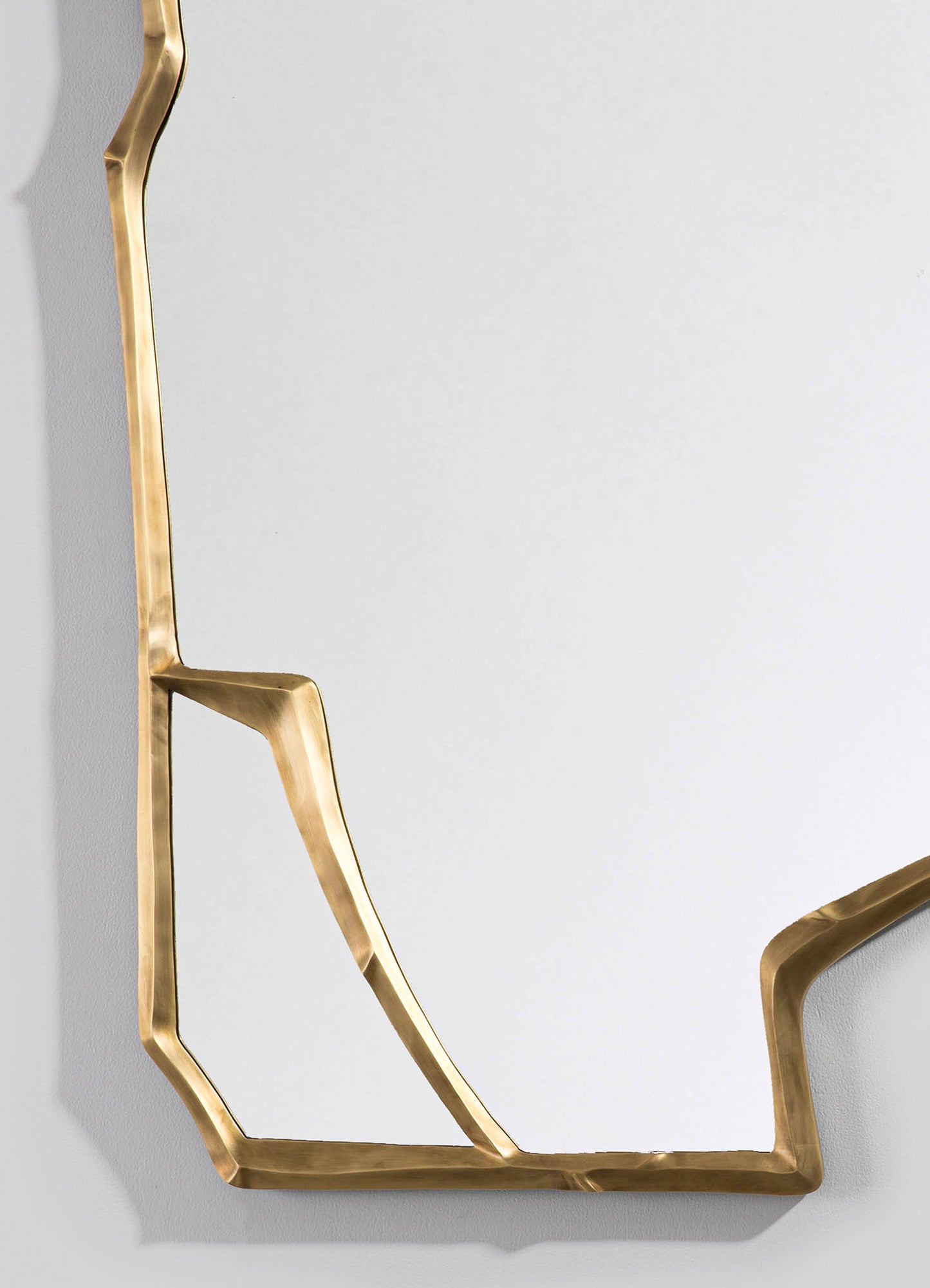 A decorative mirror with a unique geometric brass frame featuring a wavy, organic design, mounted on a neutral-colored wall.