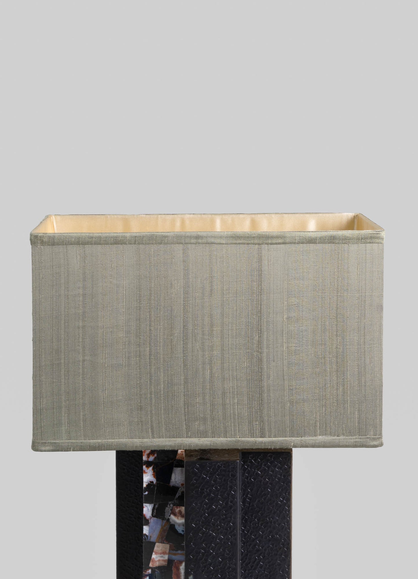 Textured beige fabric lampshade with vertical subtle stripes, lined with a smooth light-colored material, mounted on a dark base with a mosaic or patterned surface.