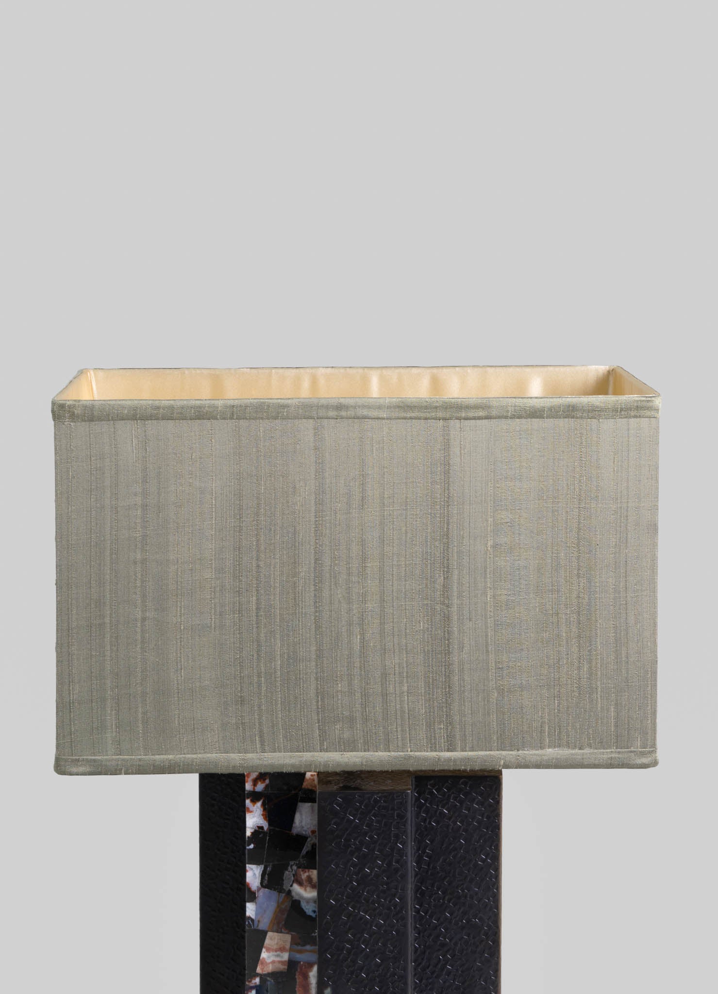 Textured beige fabric lampshade with vertical subtle stripes, lined with a smooth light-colored material, mounted on a dark base with a mosaic or patterned surface.