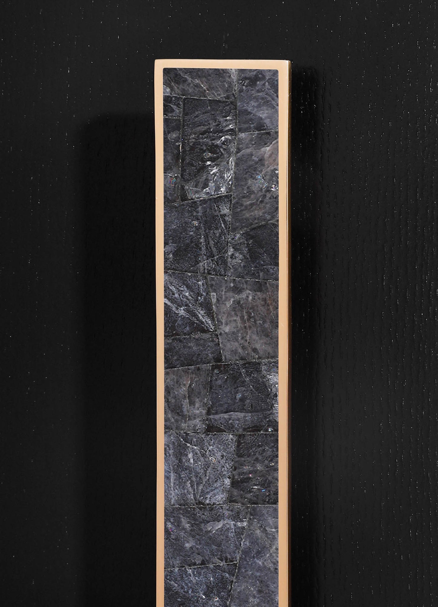 A tall, rectangular mirror with a slim, beige frame mounted on a black textured wall, featuring a reflective glass surface.